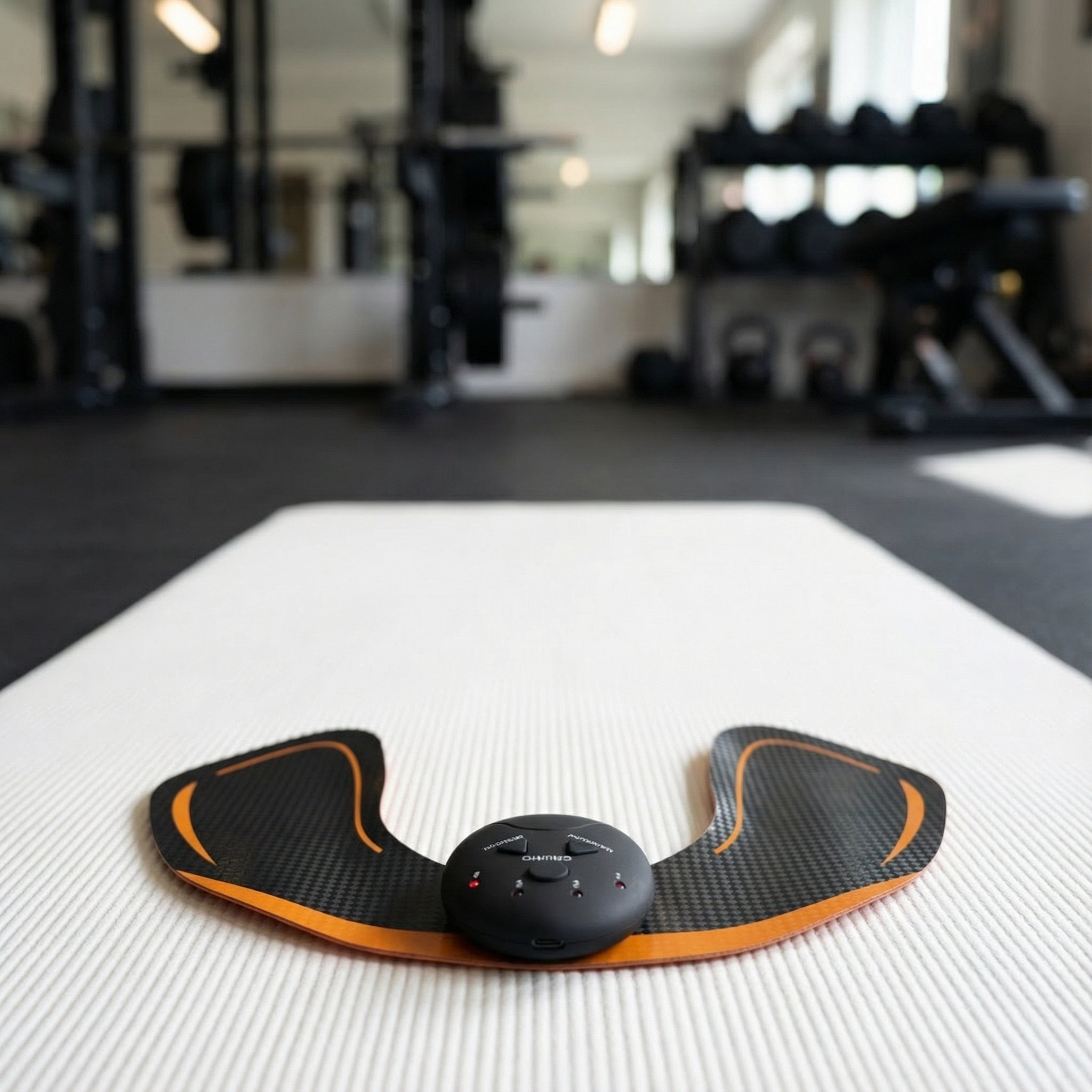 Un entrenador muscular EMS con unidad de control negra sobre una alfombra blanca en un gimnasio.