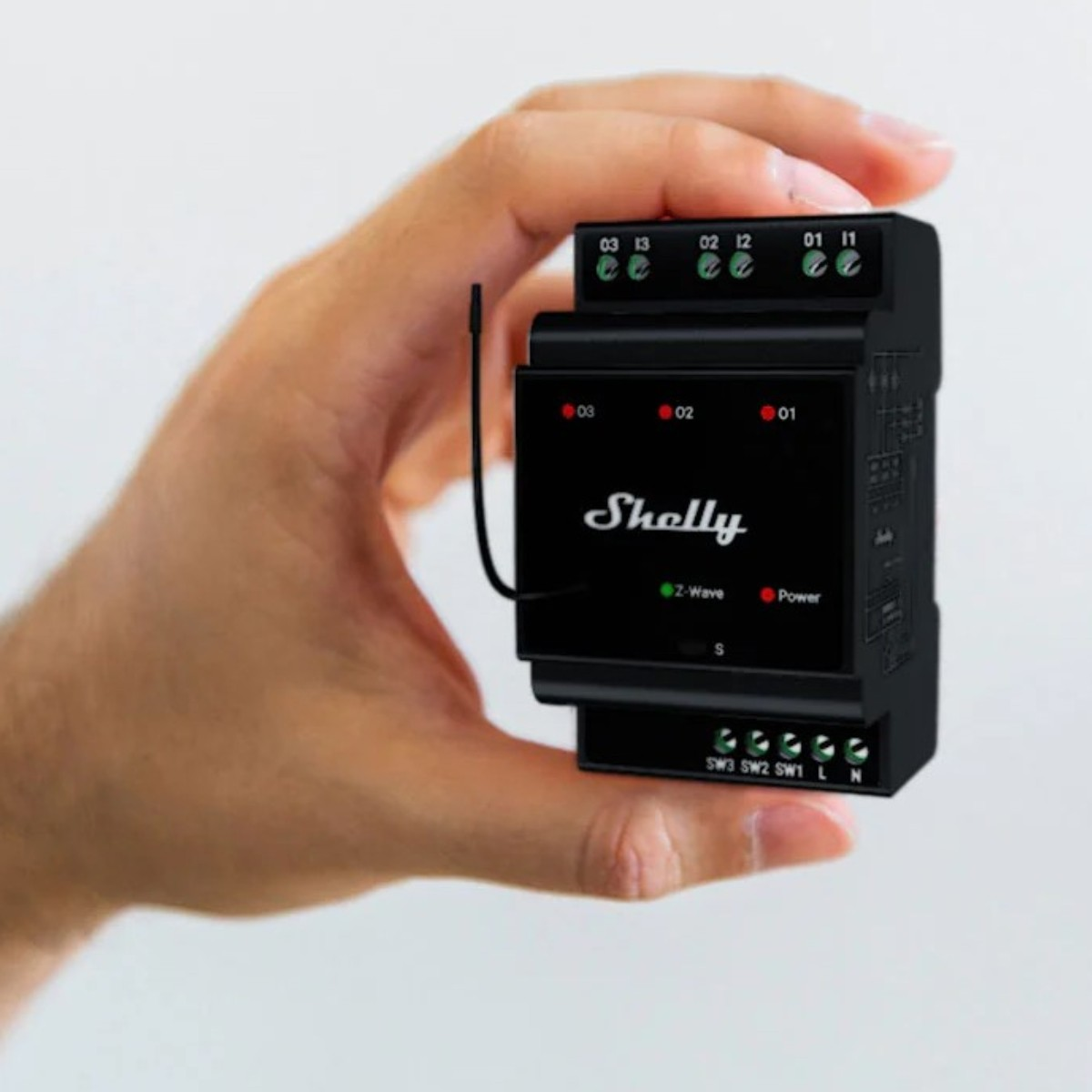 Dłoń trzyma małe czarne urządzenie Shelly Z-Wave z anteną i zaciskami.