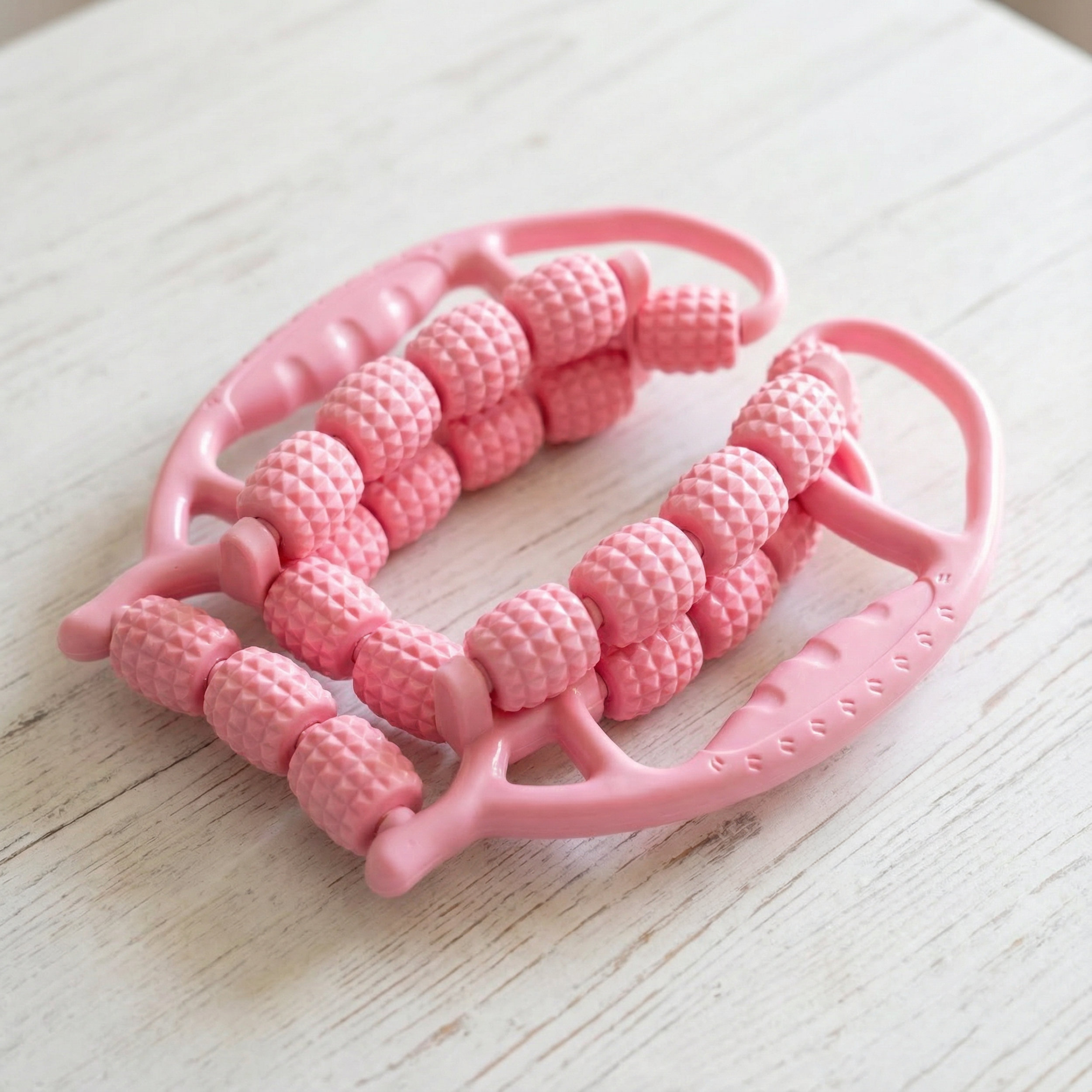 Un rodillo de masaje rosa con mangos y rodillos como cuentas sobre una mesa de madera.