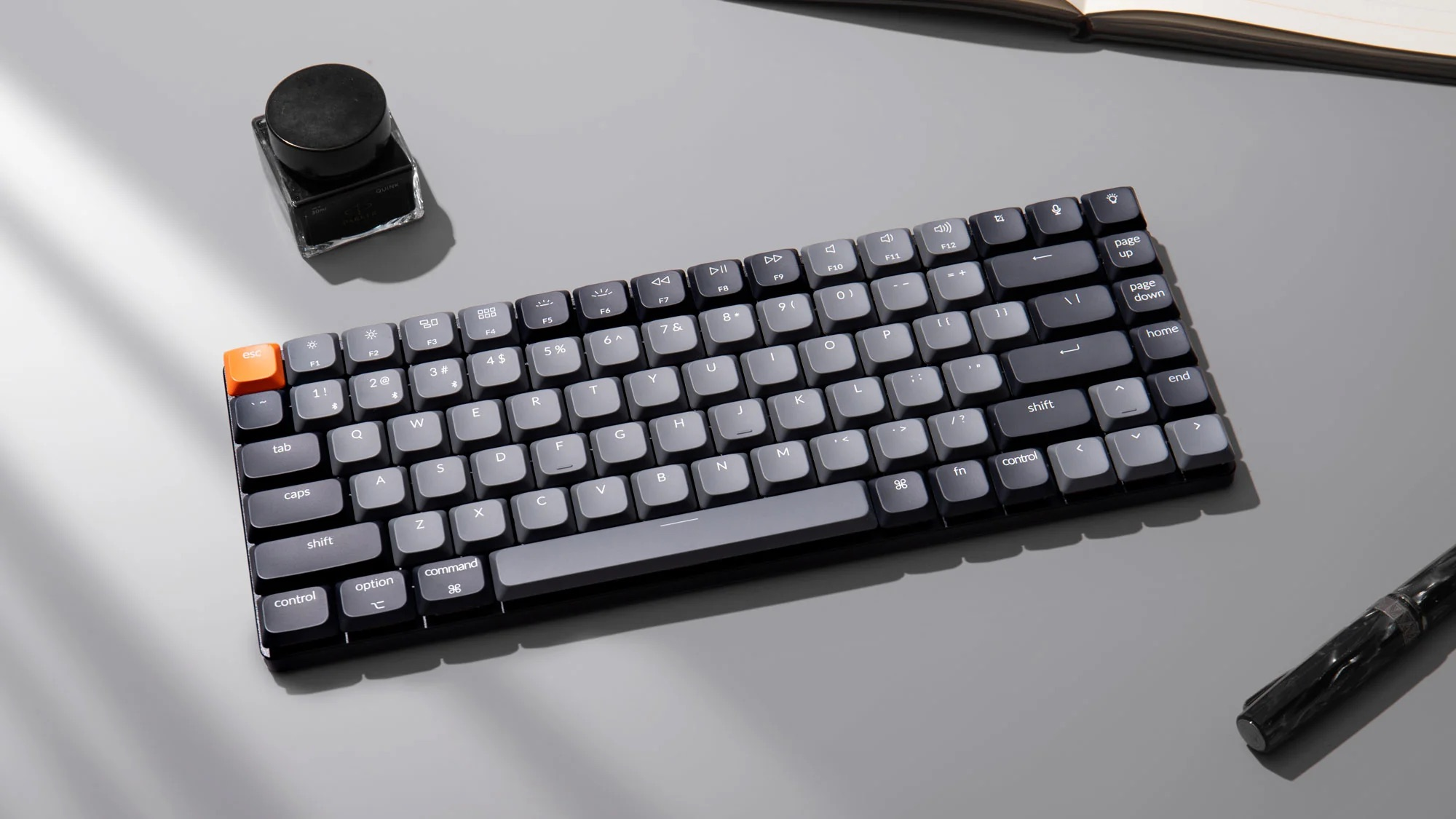 Ciemnoszara klawiatura mechaniczna z pomarańczowym klawiszem ESC na szarej powierzchni.