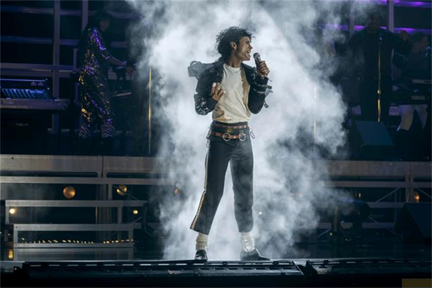 Michael Jackson singt auf einer Bühne mit viel Rauch, trägt eine Jacke und Hose.