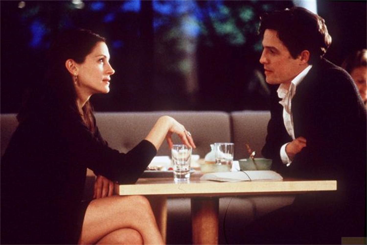 Un uomo e una donna siedono uno di fronte all'altro a un tavolo. Sono vestiti elegantemente.