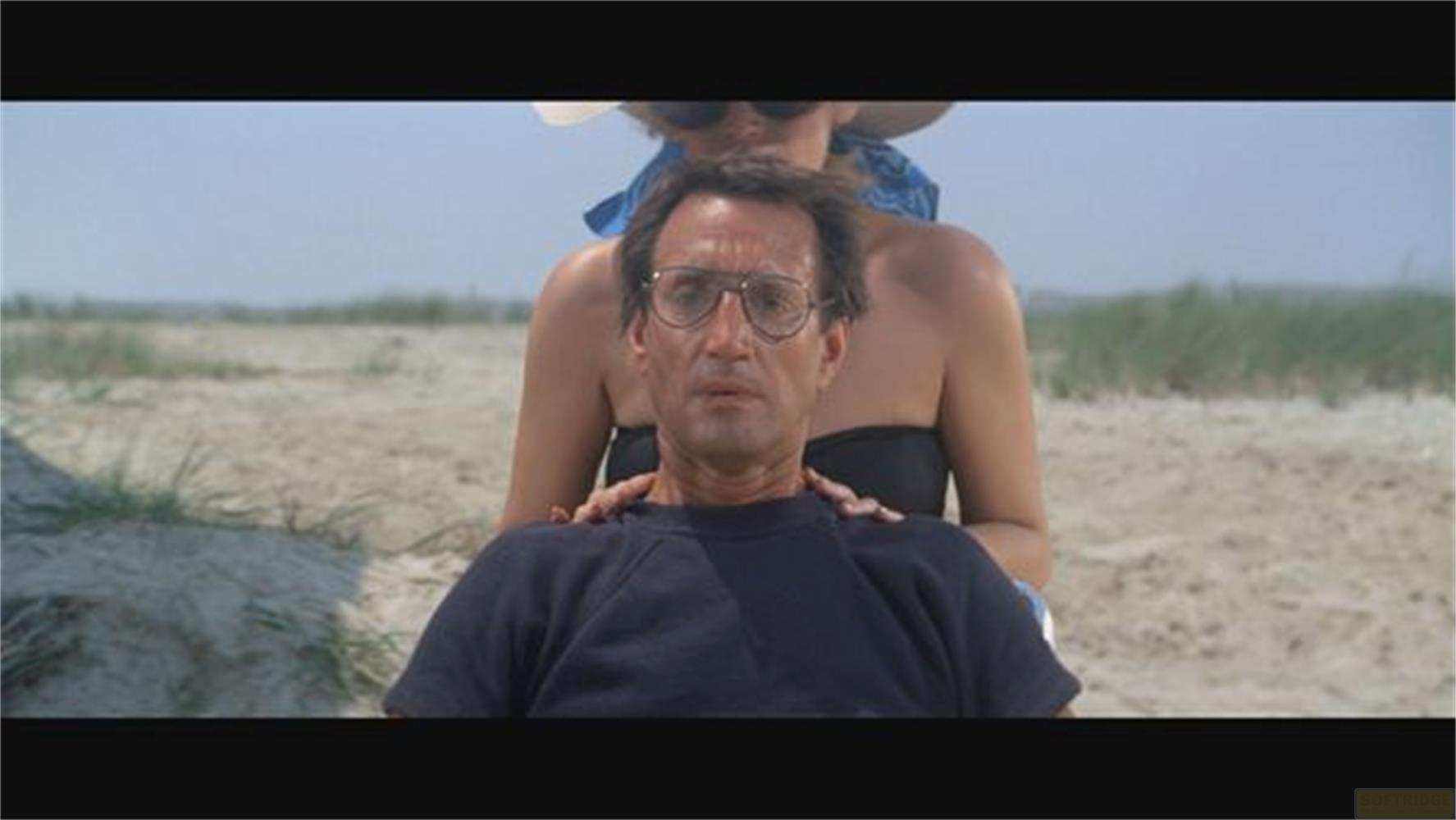 Mann mit Brille am Strand, Frau hinter ihm.