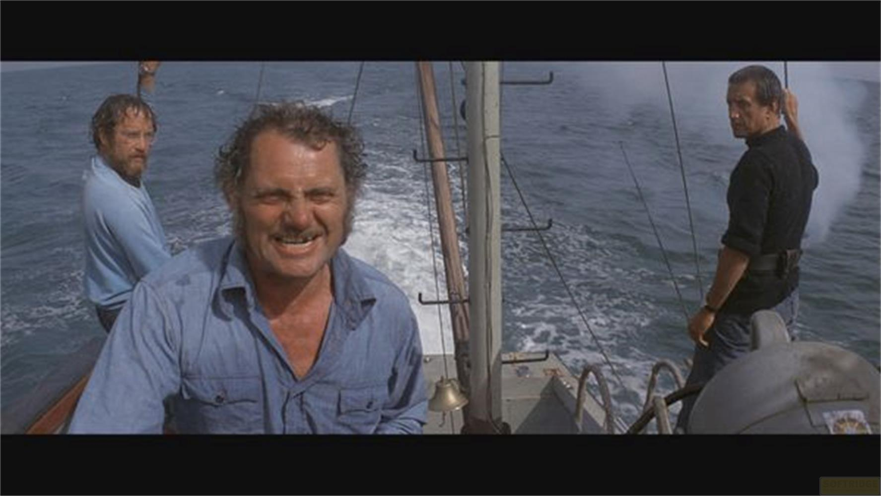 Drei Männer auf einem Boot im Meer, einer lacht, zwei schauen zur Seite.