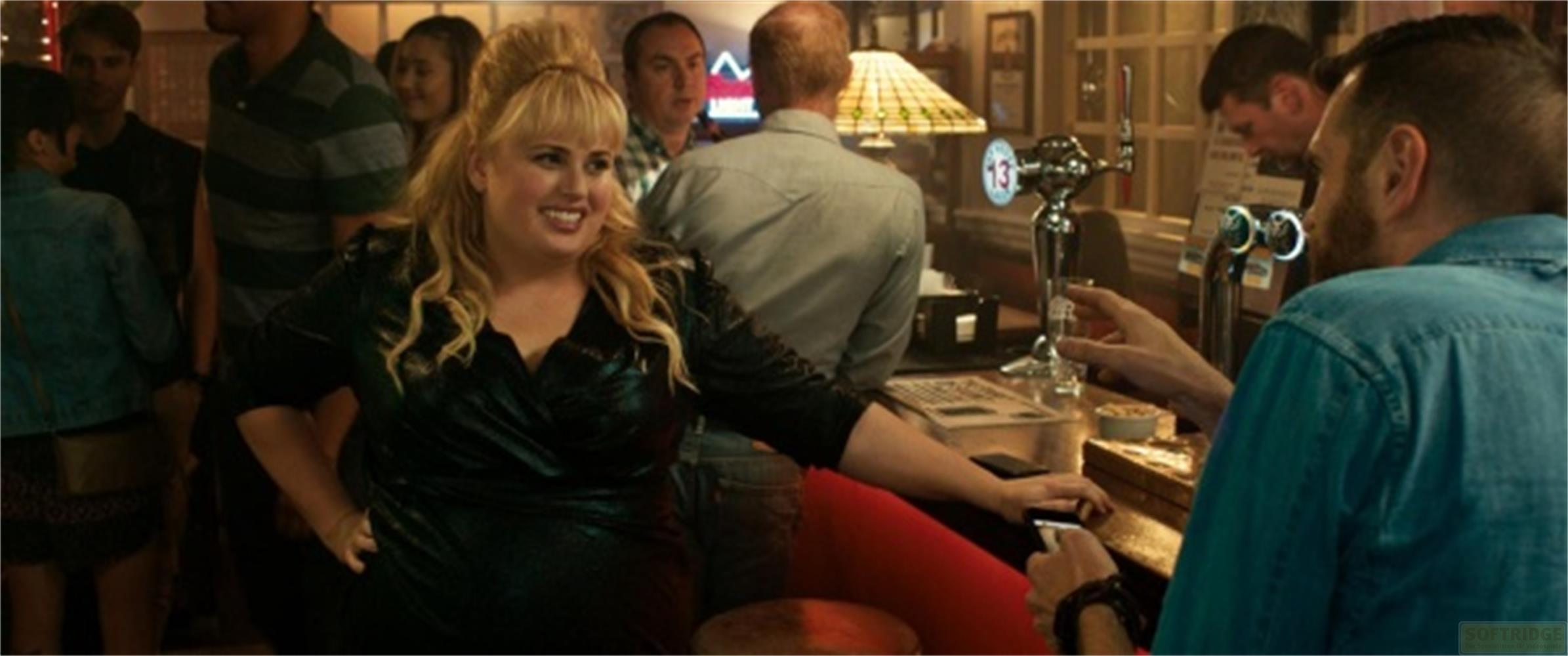 Eine Frau mit blondem Haar im Vordergrund, in einem Pub oder einer Bar mit anderen Leuten.