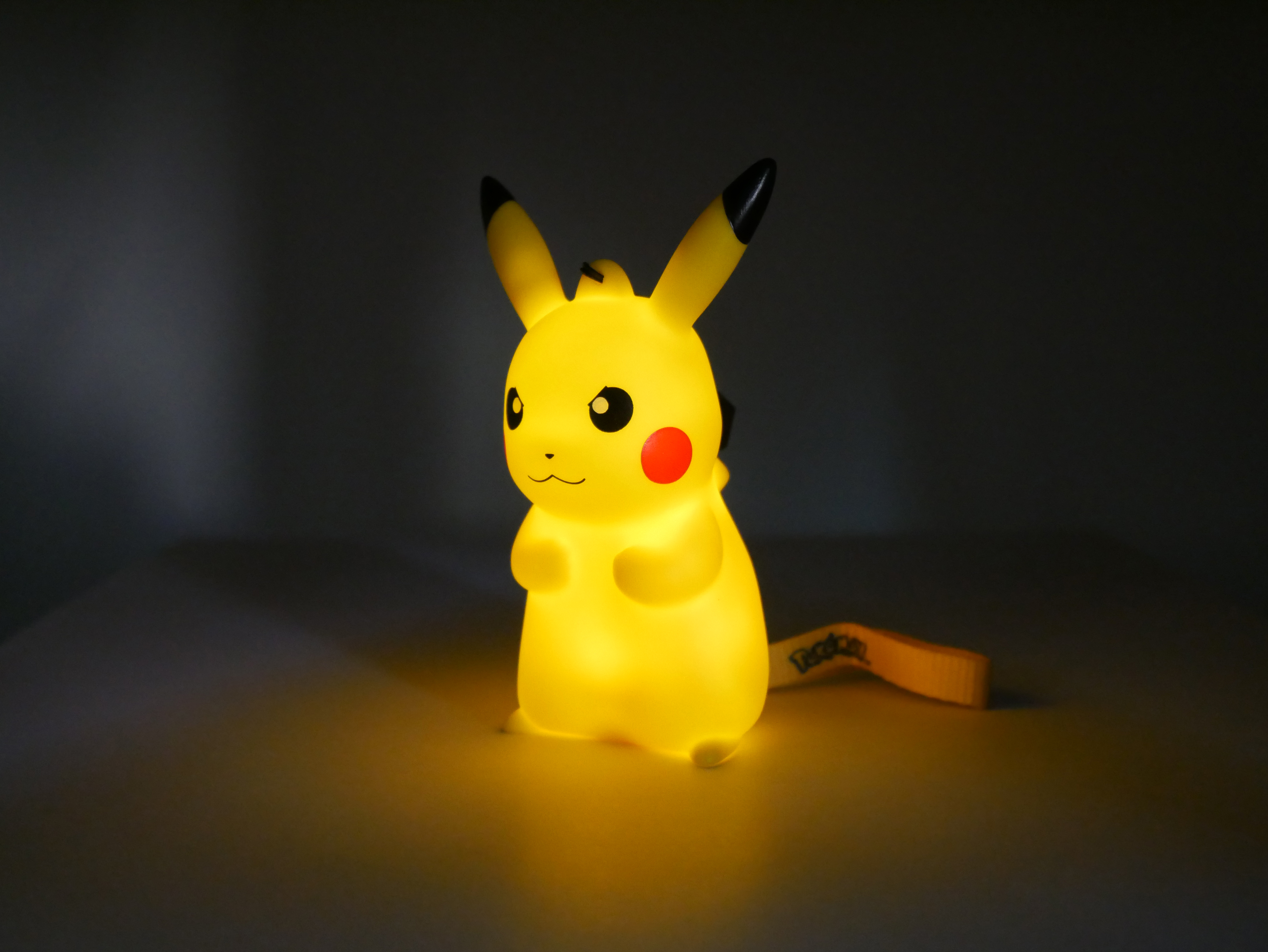 Eine leuchtende gelbe Pikachu-Figur mit schwarzen Ohrspitzen steht im Dunkeln.