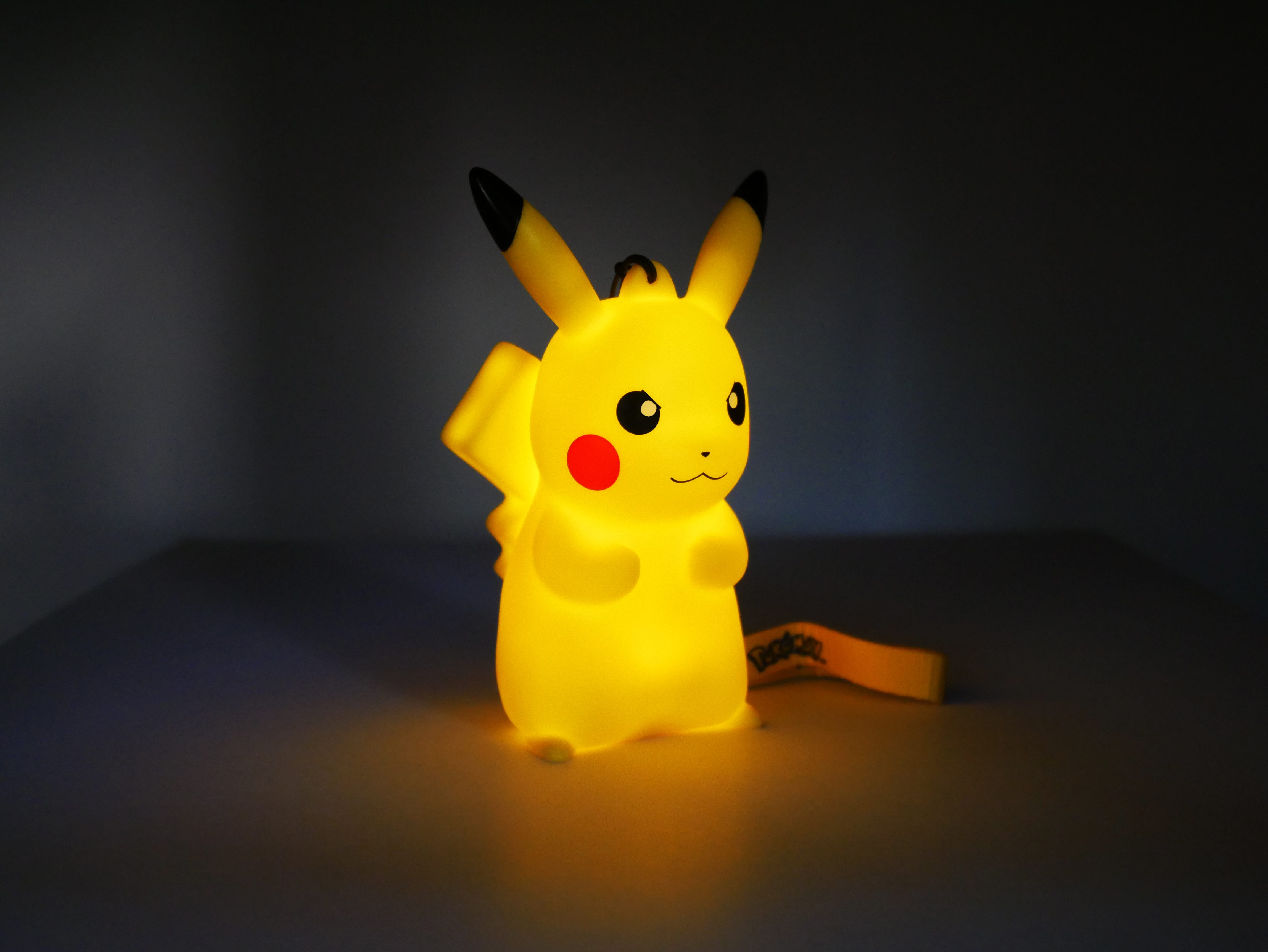 Eine leuchtende gelbe Pikachu-Figur mit roten Wangen und schwarzen Ohrenspitzen steht auf einer dunklen Oberfläche.