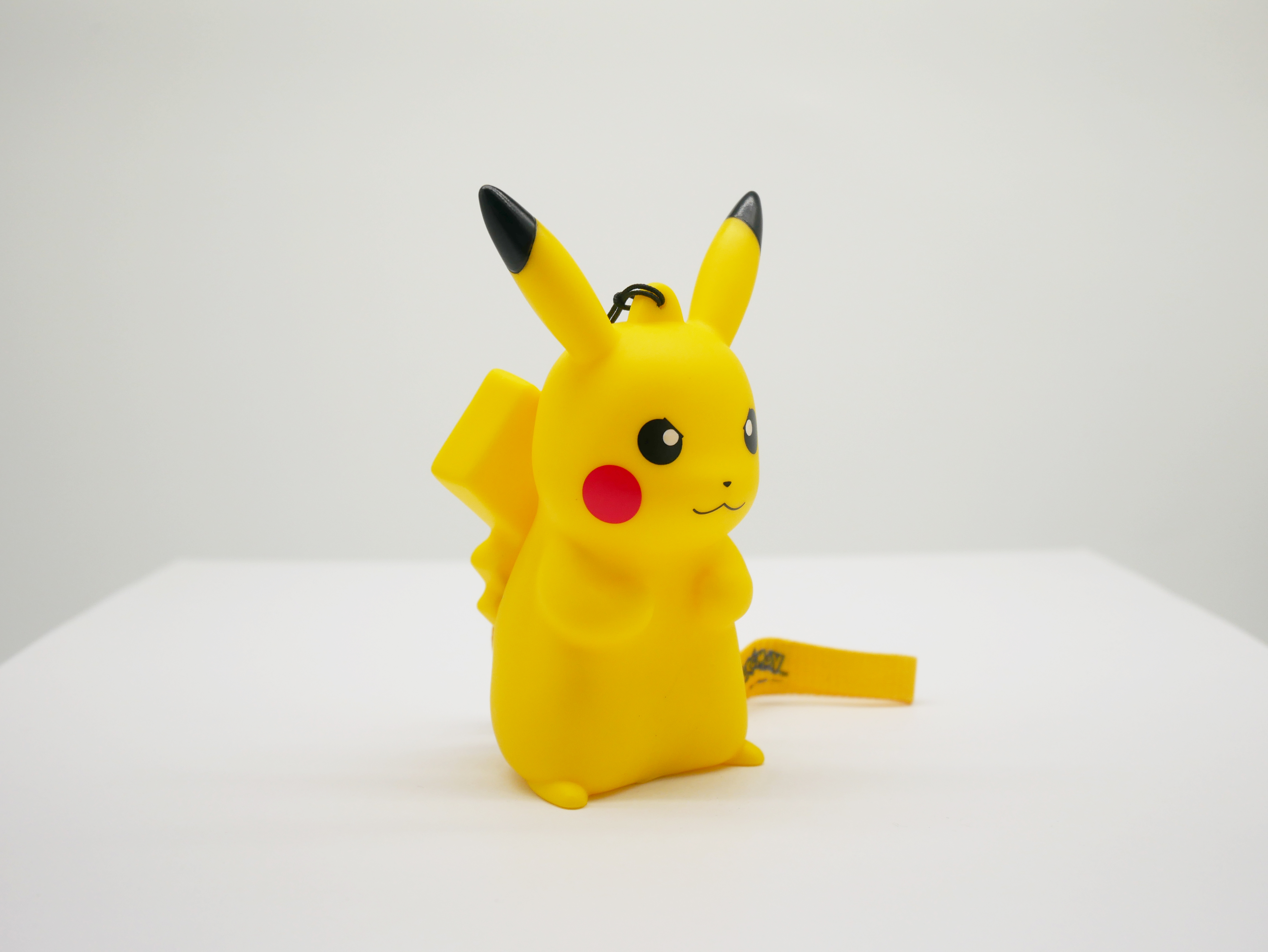 Ein gelbes Pikachu-Spielzeug mit schwarzen Ohrenspitzen und roten Wangen sitzt auf weißer Fläche.