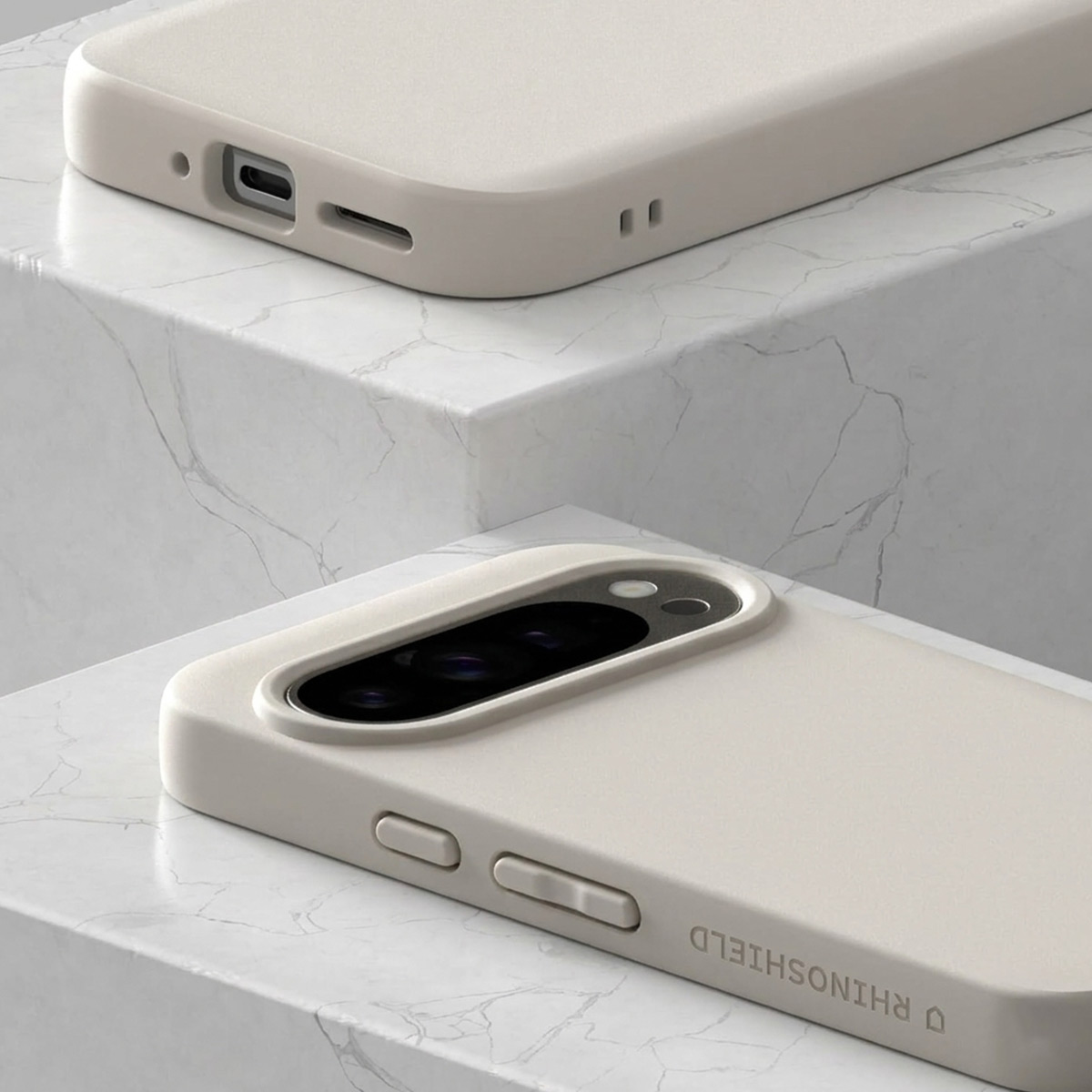 Twee lichtgekleurde telefoonhoesjes op marmeren blokken. Eén toont oplaadpoort.