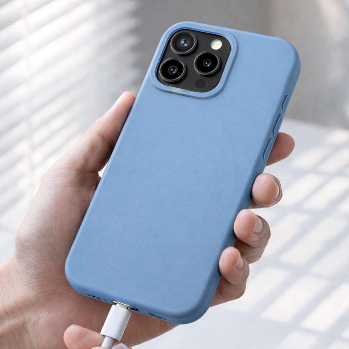 Een hand houdt een blauwe telefoonhoes met een oplaadkabel vast.