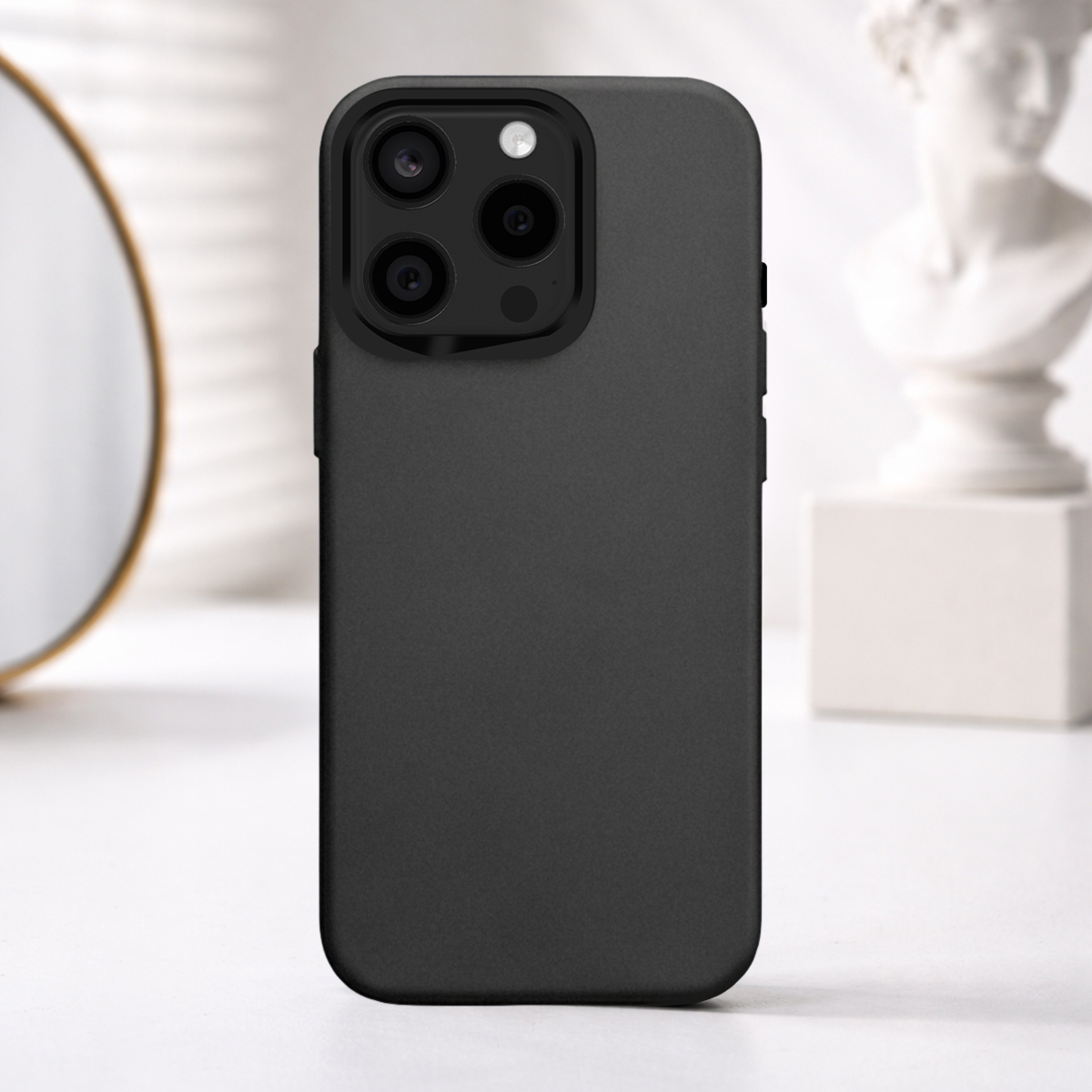 Un téléphone noir avec appareil photo, sur une table, avec miroir et statue en arrière-plan.