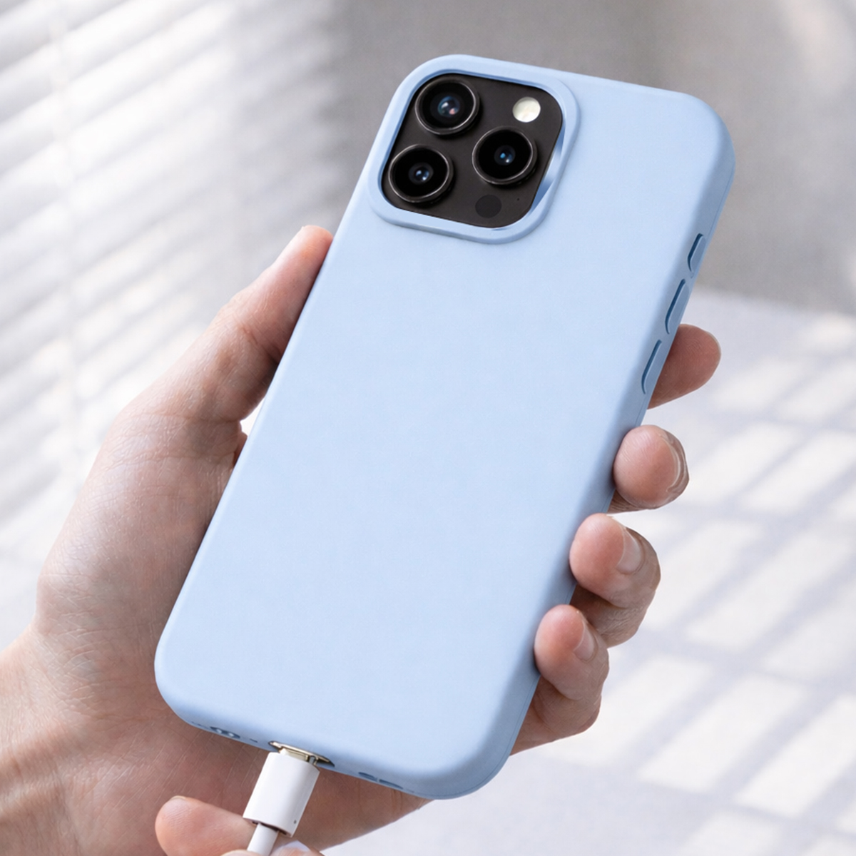 Une main tient un téléphone bleu clair avec câble de chargement, gros plan.