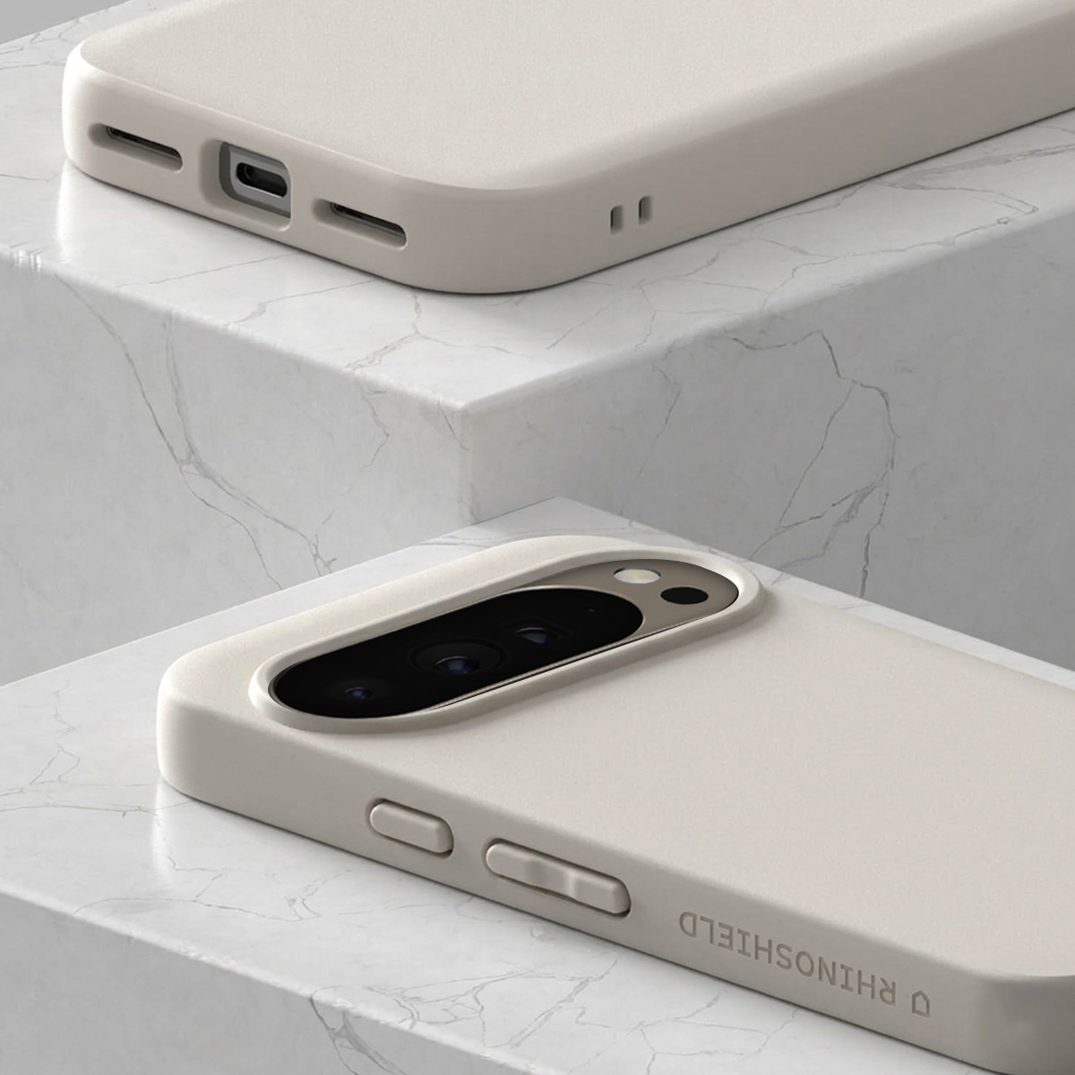 Deux coques de téléphone beige clair sur marbre. L'une montre le port de charge, l'autre le renflement de l'appareil photo.