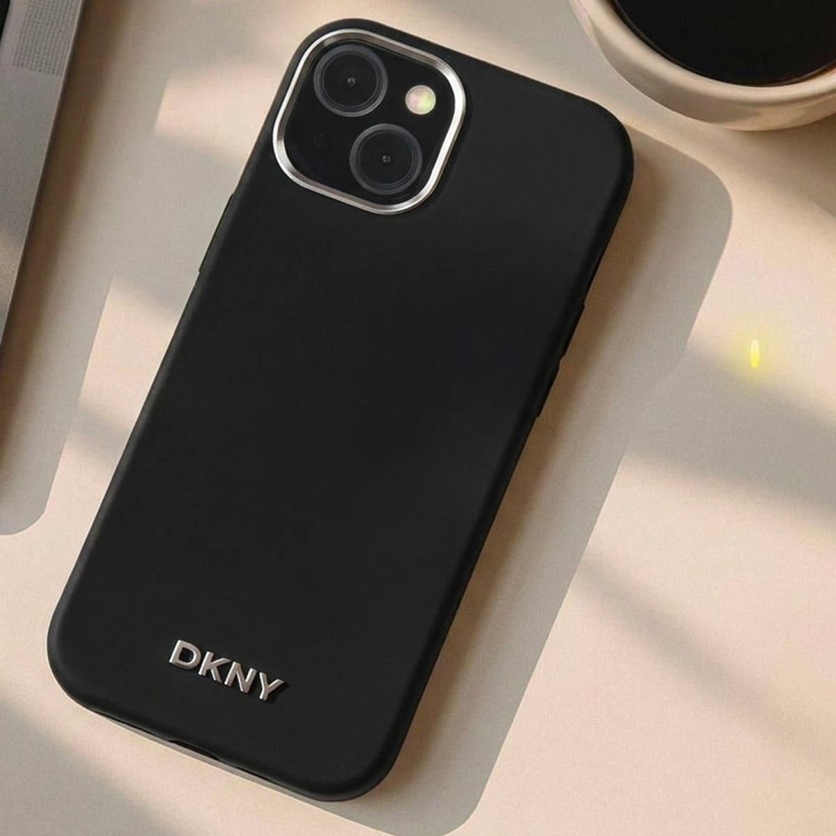 Custodia nera per telefono con logo DKNY e lenti fotocamera, su superficie chiara.