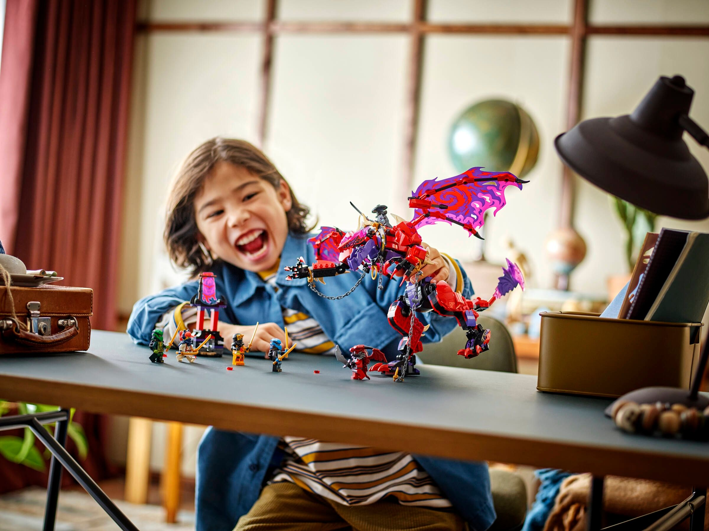 Ein Junge spielt mit Lego-Figuren und einem roten Drachen auf einem Schreibtisch.