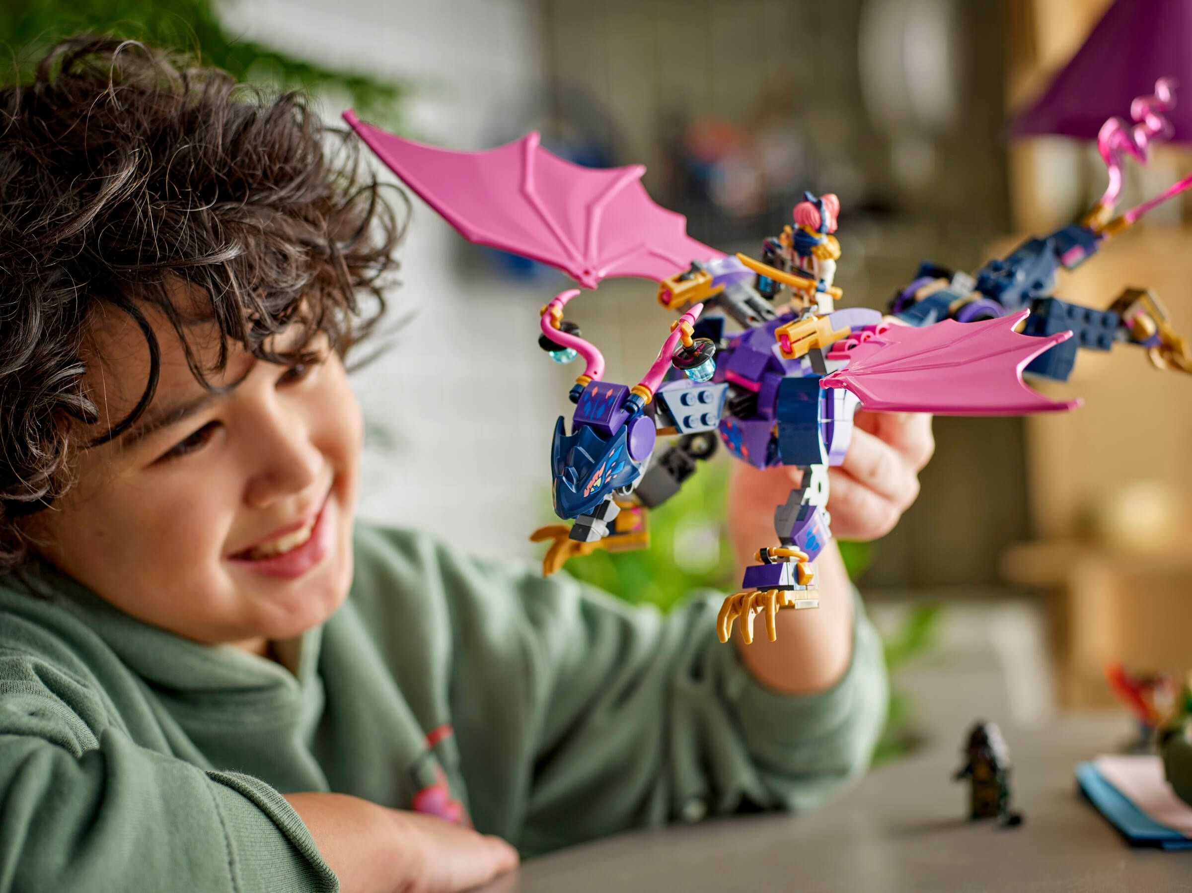 Junge hält ein farbenfrohes Lego-Drachenspielzeug mit pinken Flügeln.