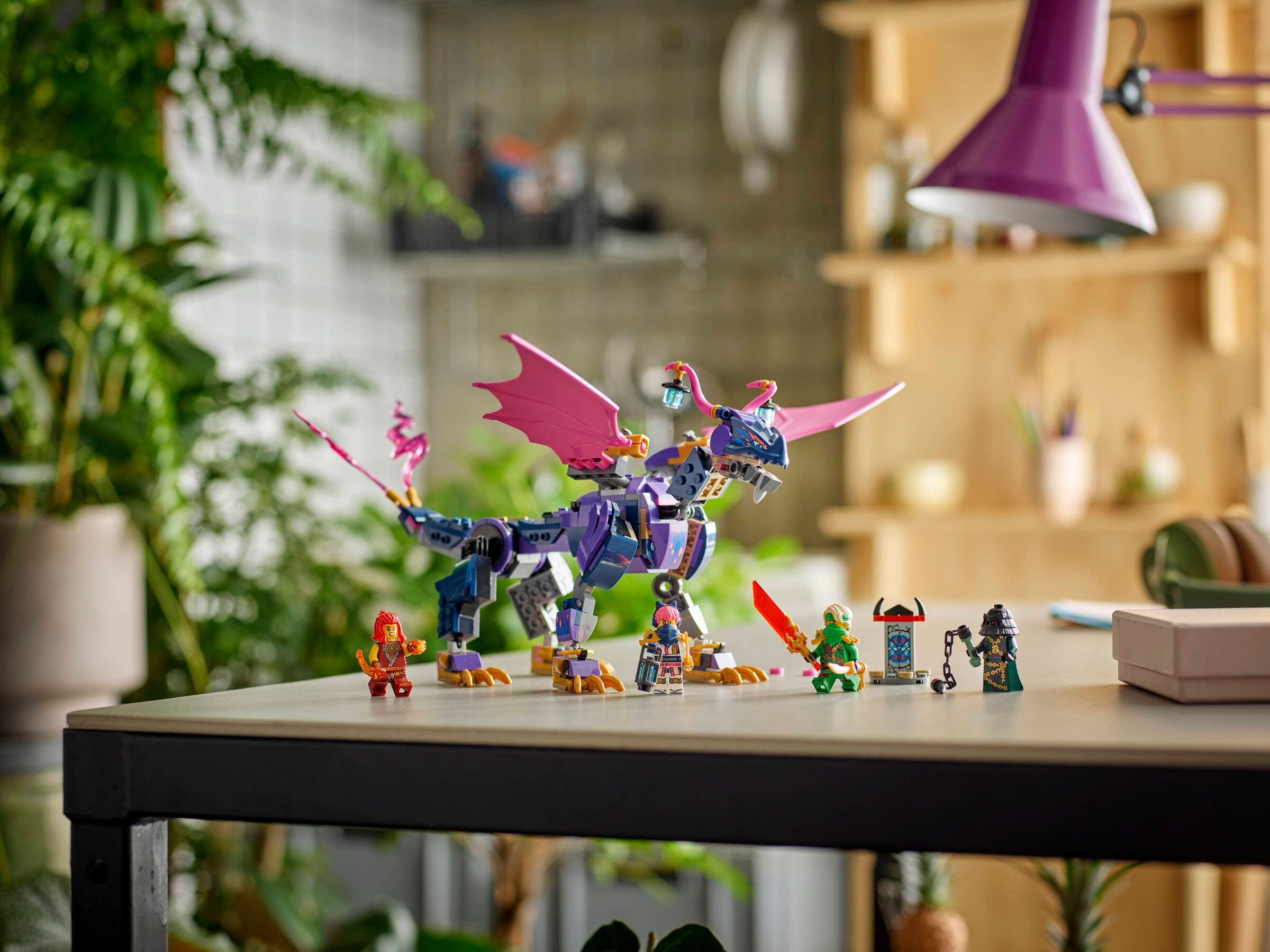 Lila Lego-Drache mit rosa Flügeln, umgeben von Lego-Figuren auf einem Tisch.