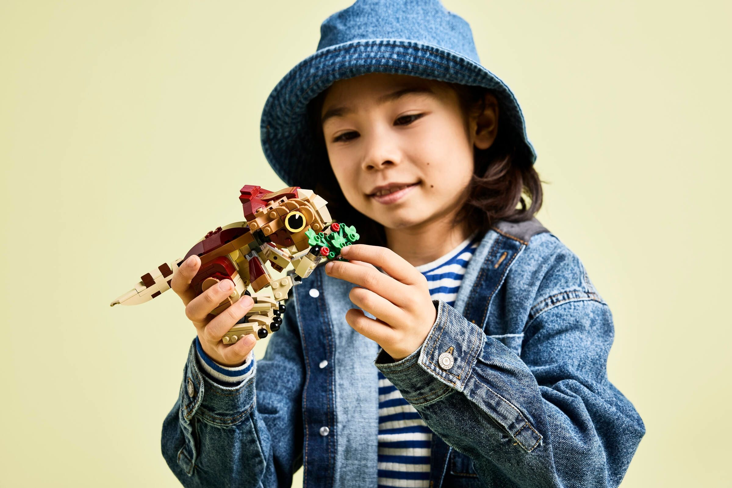Ein Kind mit einem blauen Fischerhut hält ein Lego-Modell eines Tieres.