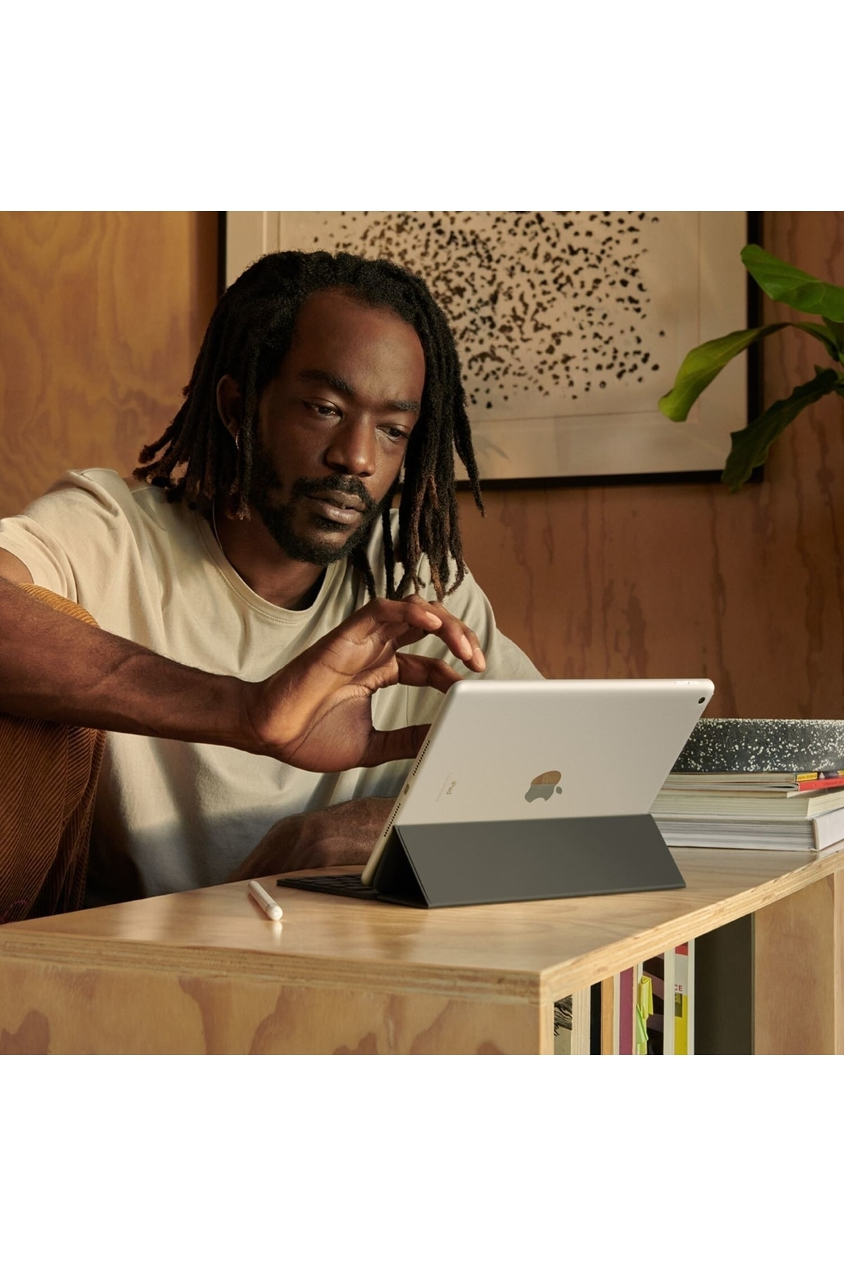 Dreadlock'lu bir adam ahşap bir masanın üzerinde duran gümüş bir iPad'e yazıyor.