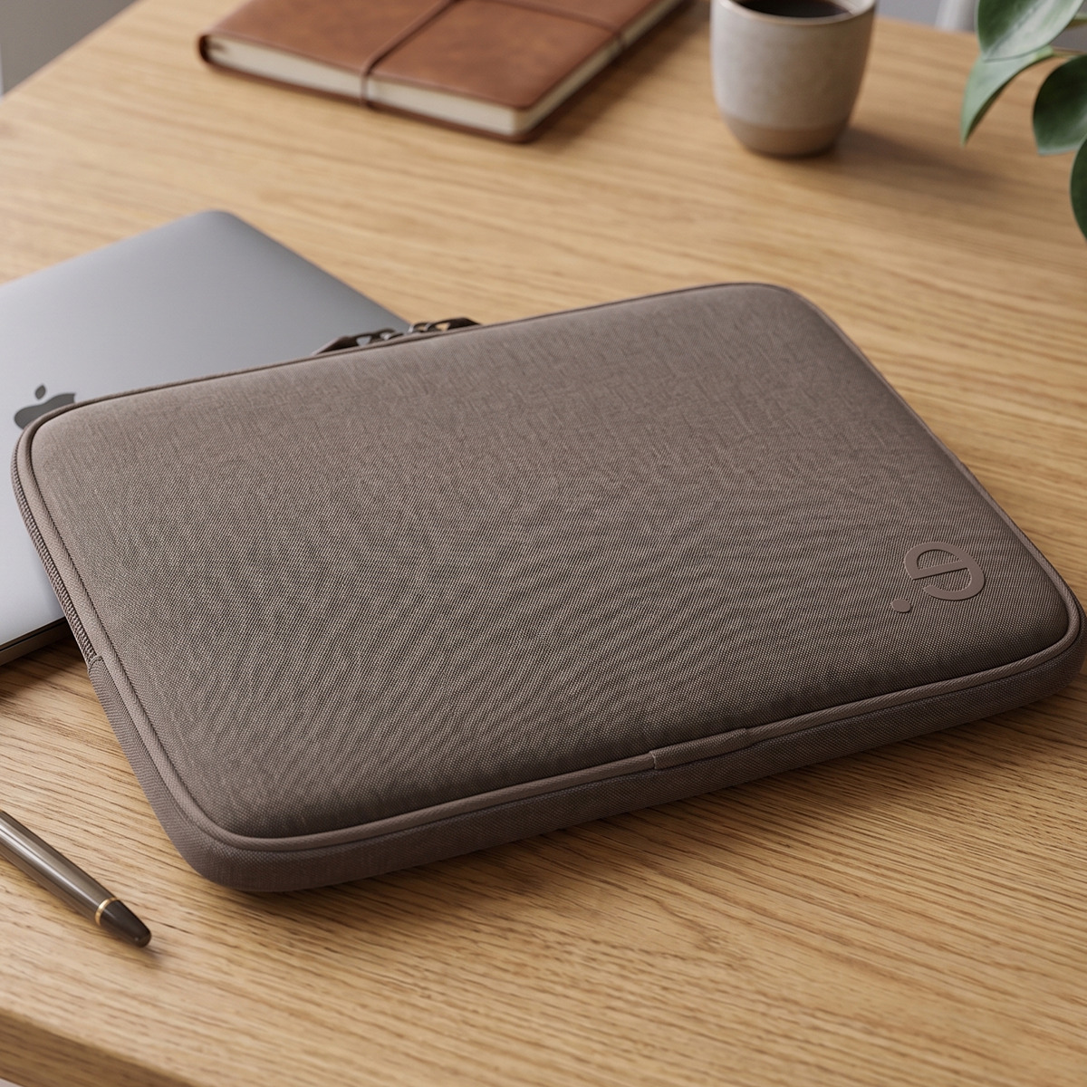 Custodia marrone per laptop su scrivania in legno con taccuino, penna e tazza.