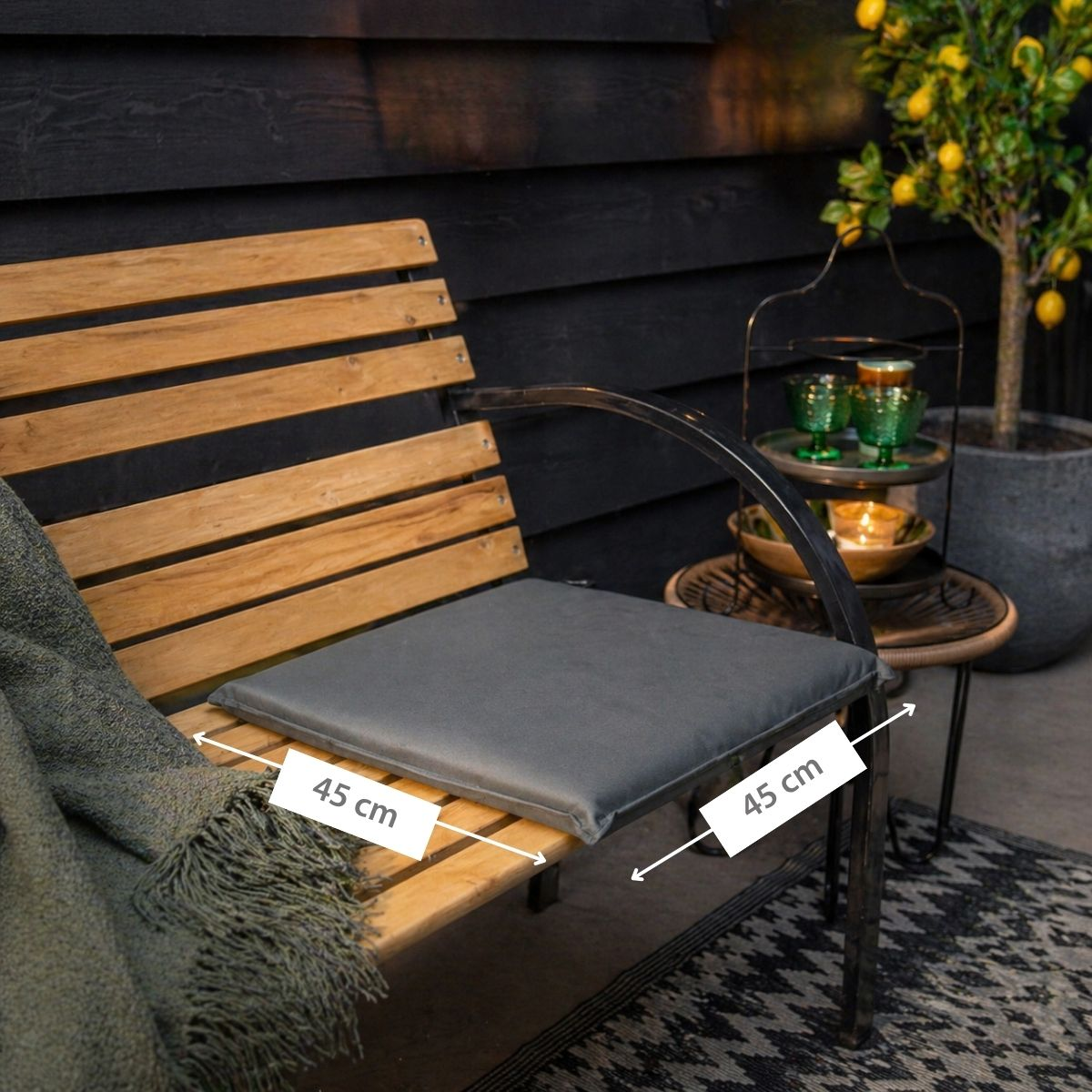 Wooden bench with dark cushion, blanket and lemon tree in background.