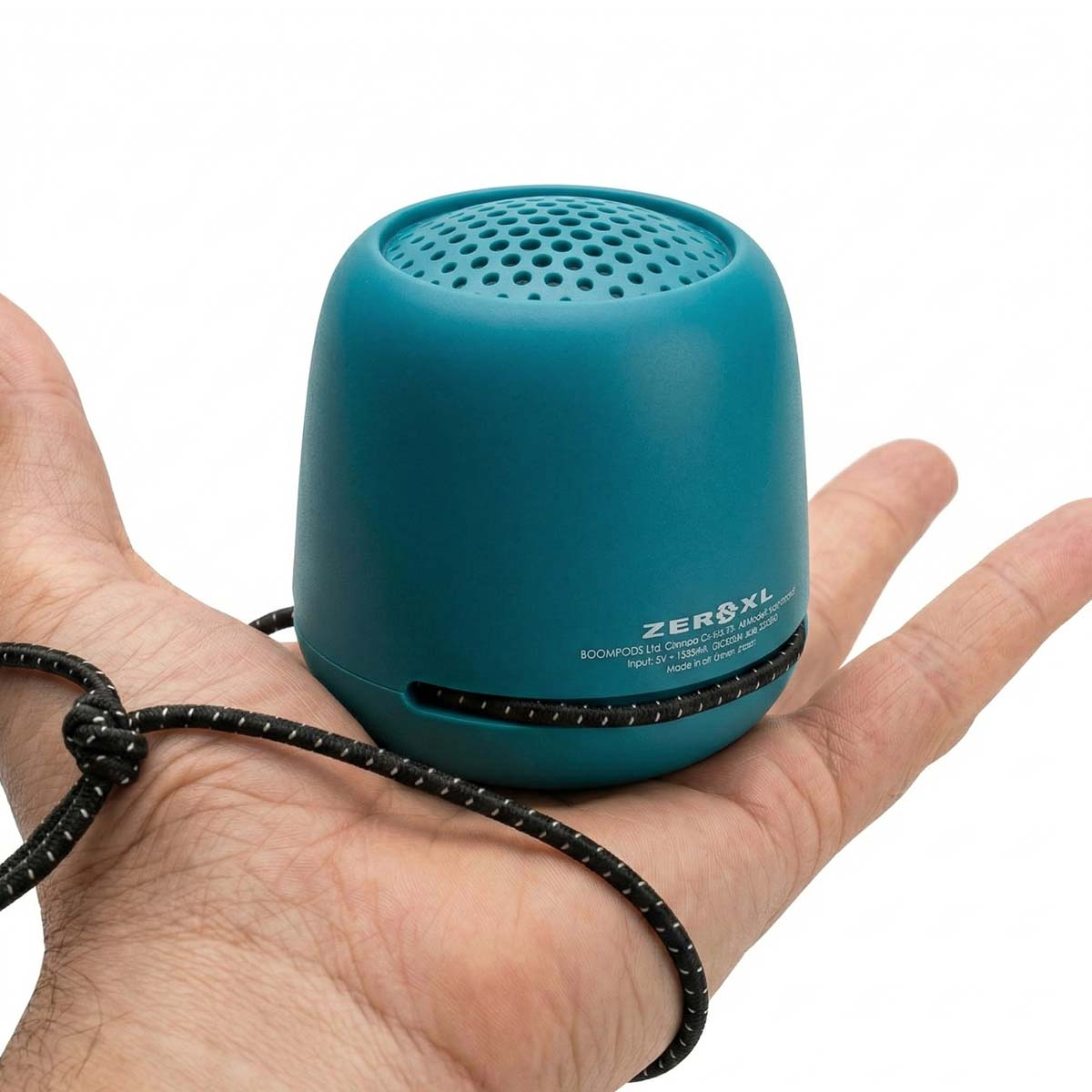 Une enceinte bleu sarcelle avec un cordon noir repose dans une main.