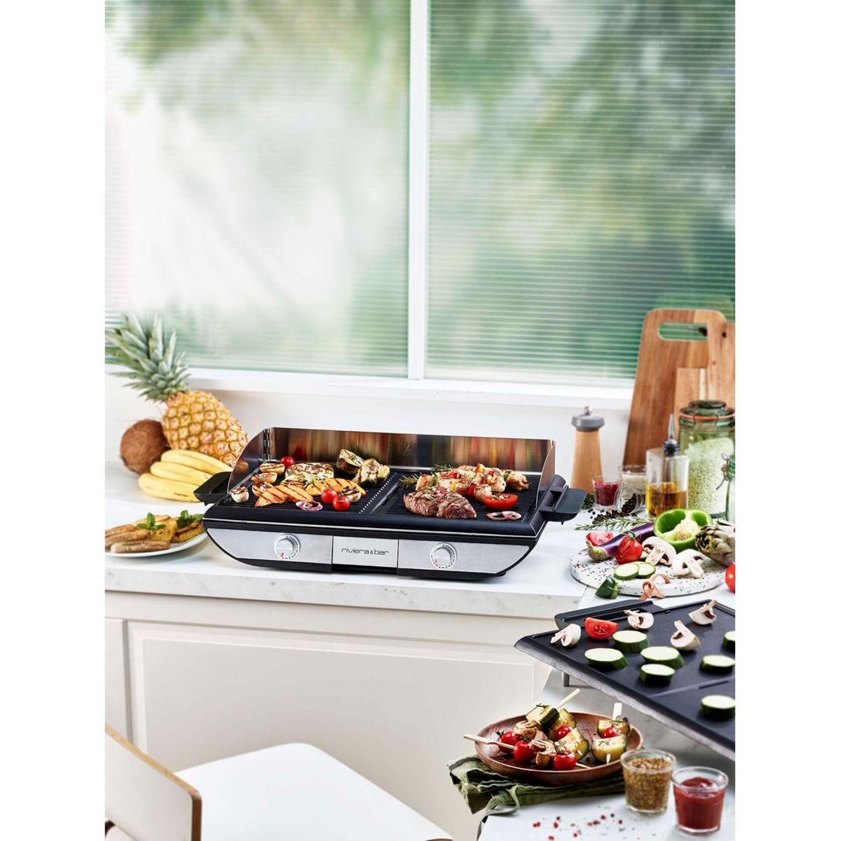 Eine Grillplatte mit Fleisch und Gemüse, frische Ananas, Bananen, Kokosnuss und gehacktes Gemüse auf einer Küchentheke.