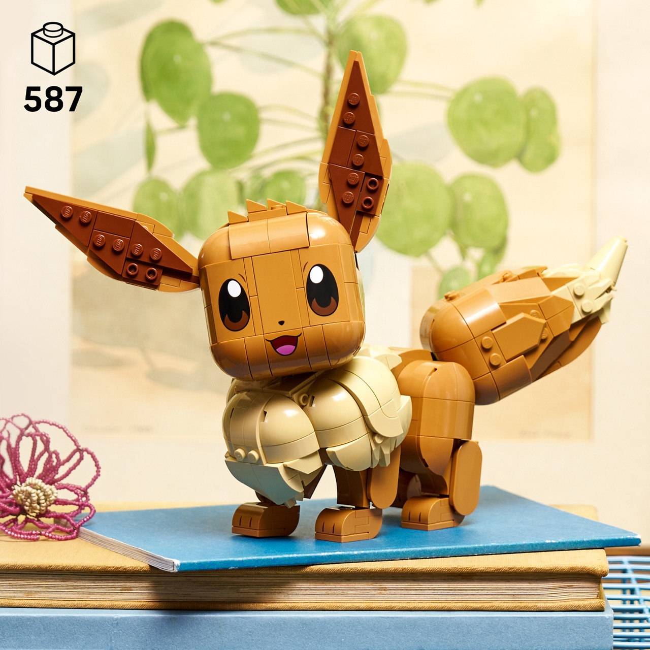 Modelo de Lego de Eevee sobre libros con decoración floral. Fondo con plantas.