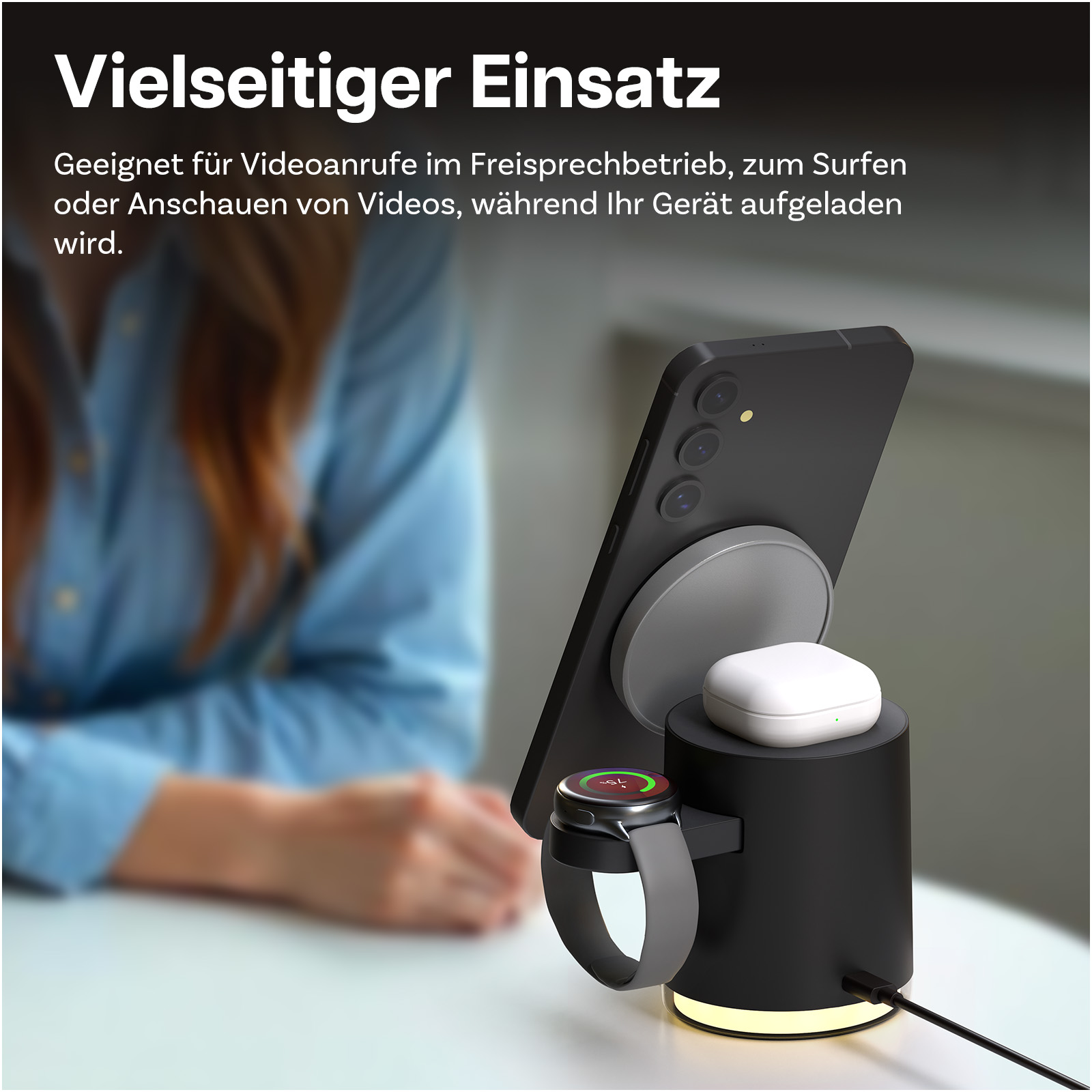Ein schwarzes Ladegerät mit Handy, Uhr und Ohrhörern. Frau im Hintergrund.