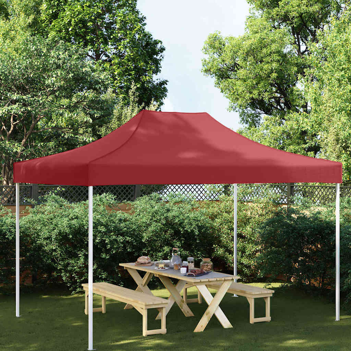 Una tettoia rossa ombreggia un tavolo da picnic con panche in un giardino.