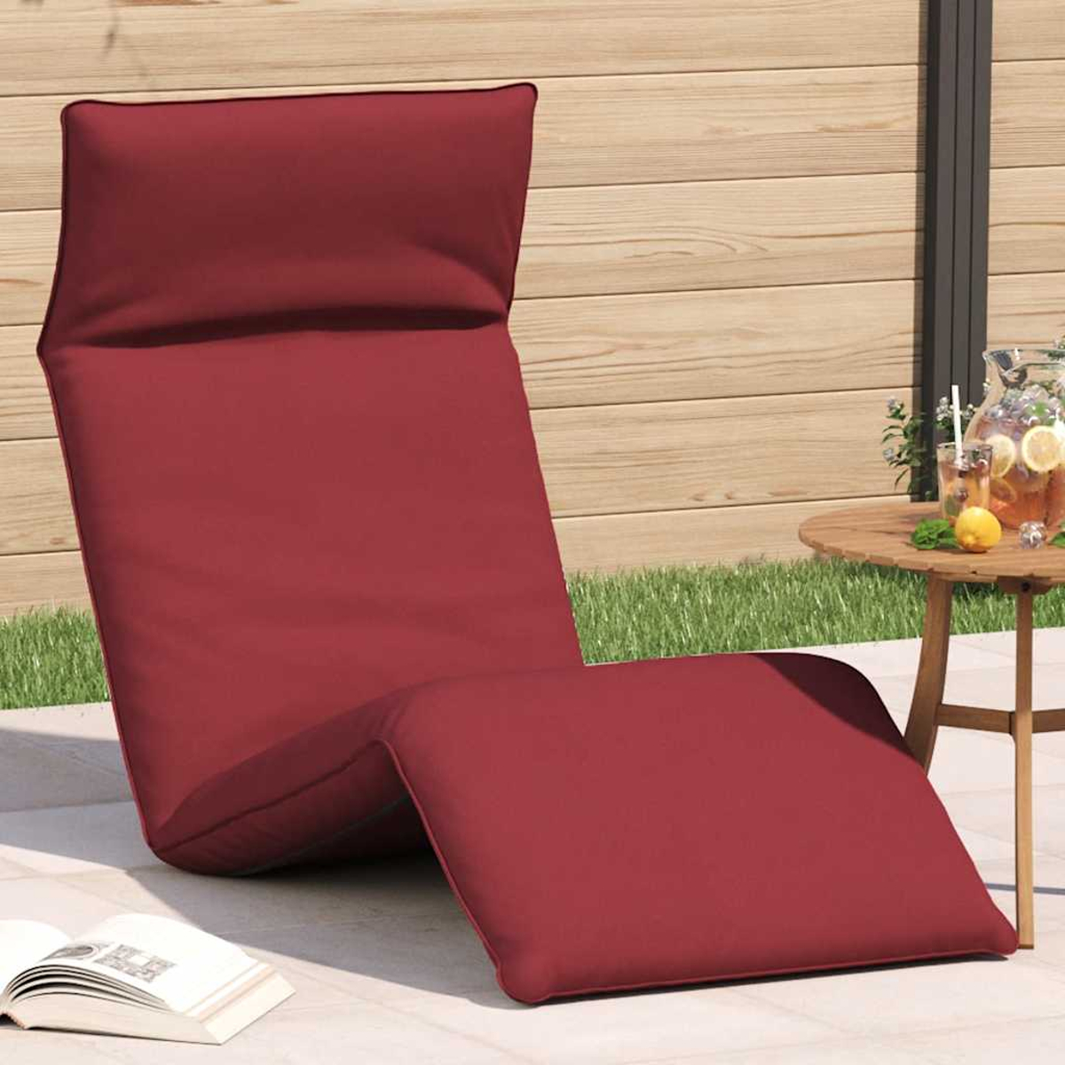 Rote Liege mit Kissen vor Holzwand, mit Getränken auf einem Tisch daneben.