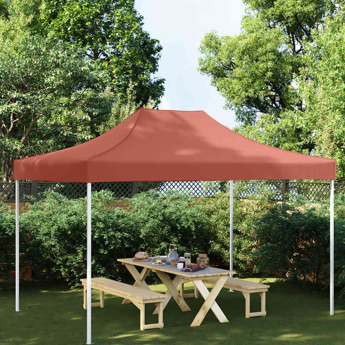 Una tenda rossa sovrasta un tavolo e panche di legno in un giardino.
