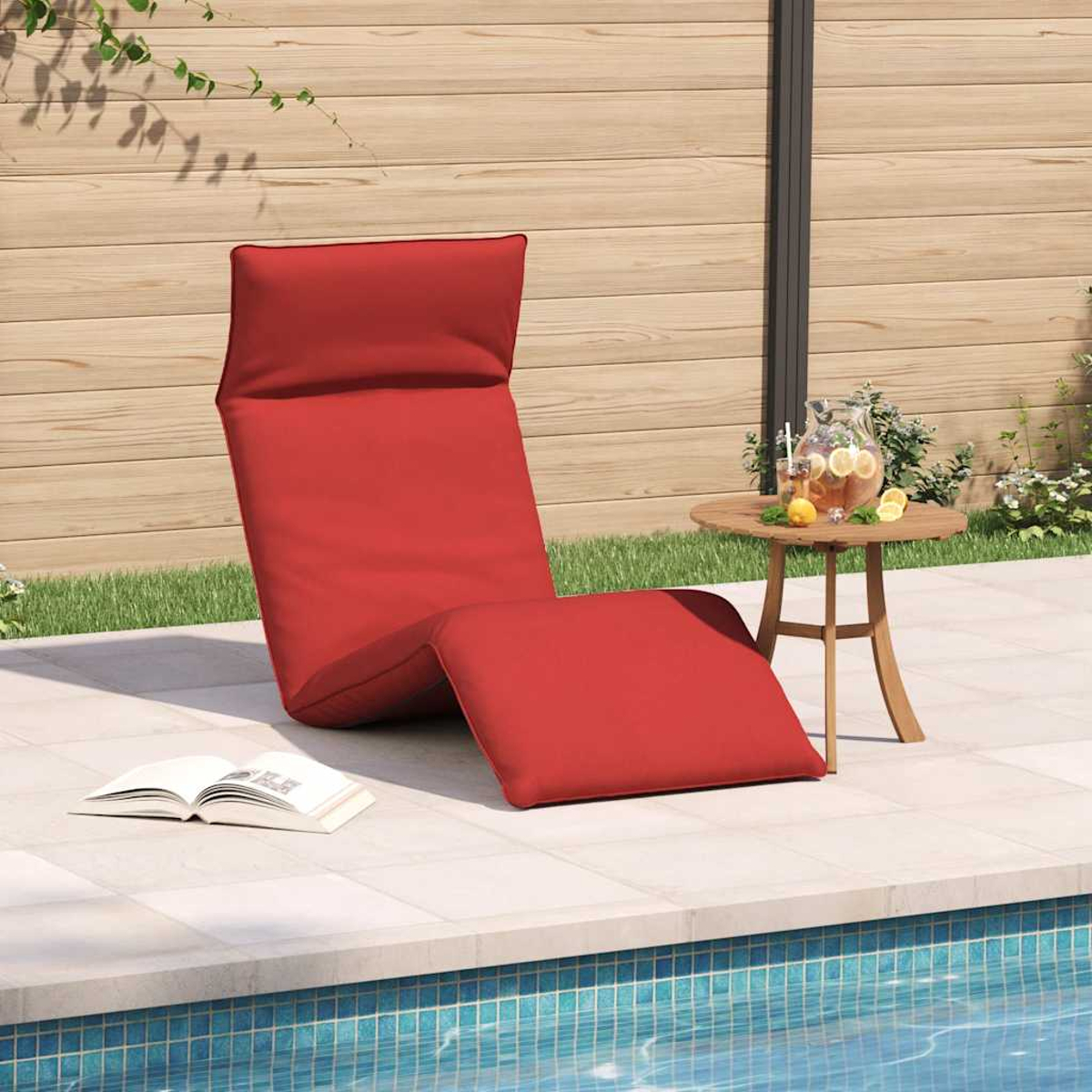Rote Liege am Pool mit Buch und Getränk auf kleinem Tisch.