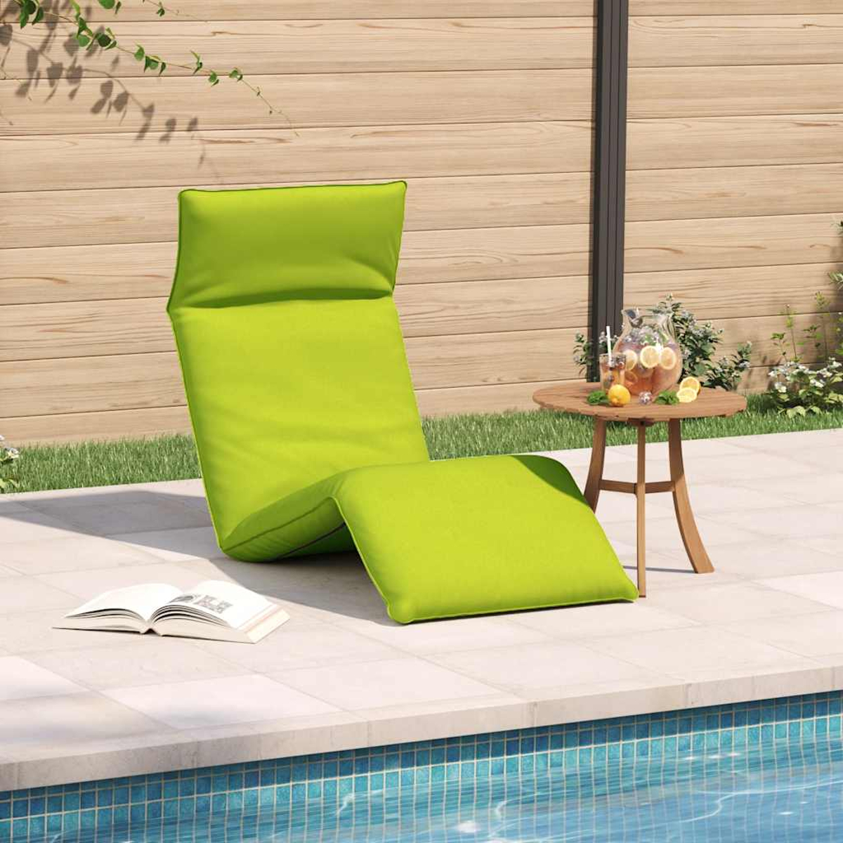 Una sedia a sdraio verde vicino a una piscina con una bevanda e un libro.