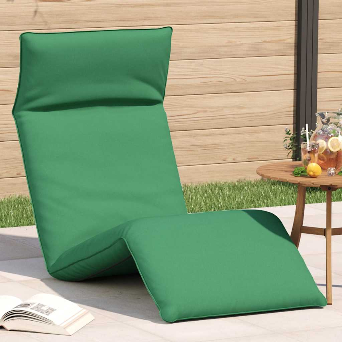 Una chaise longue verde con cuscini siede su un patio accanto a una recinzione di legno.