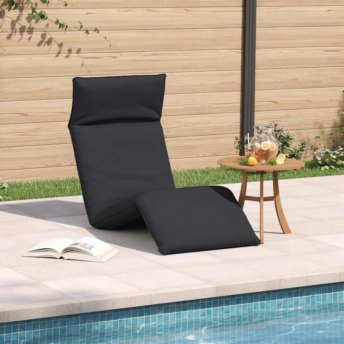Ein schwarzer Liegestuhl am Pool mit einem Buch und einem Getränk auf einem Tisch.