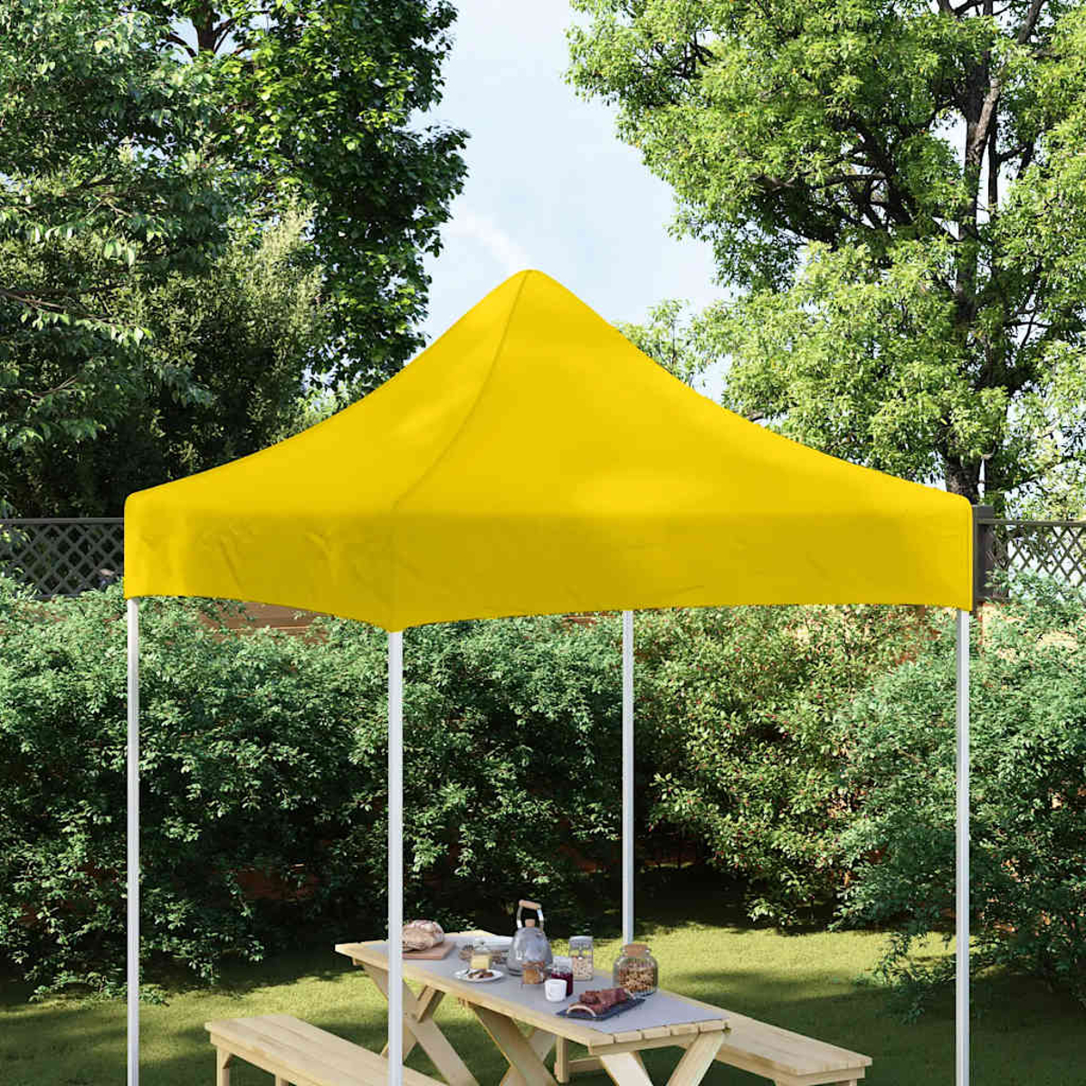 Una tenda gialla con tavolo da picnic e panche in un giardino.