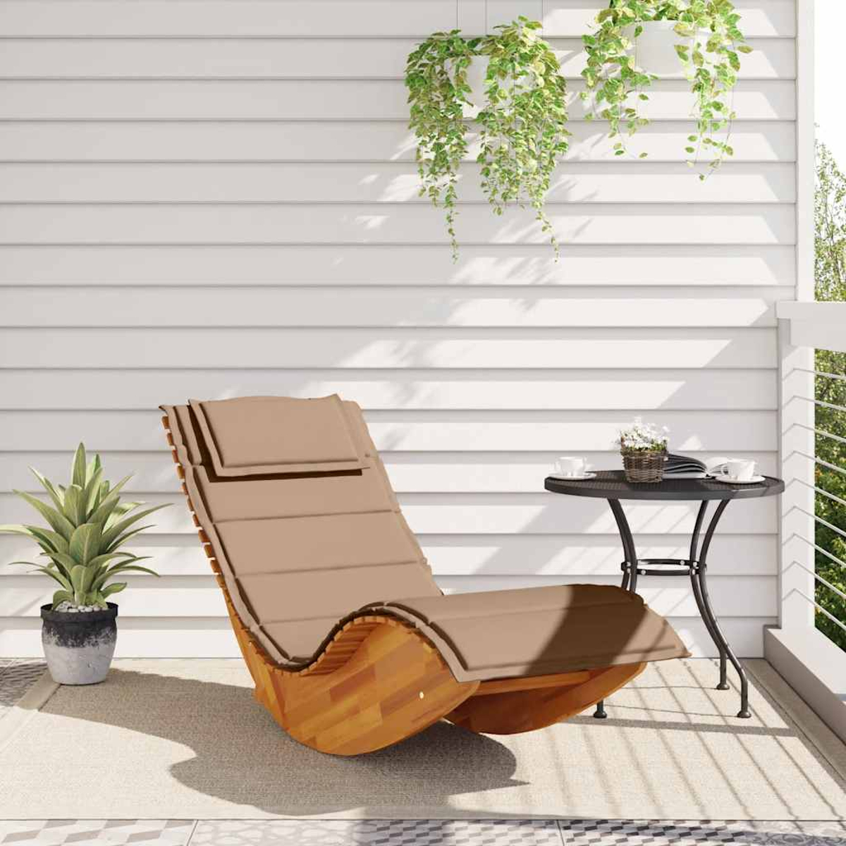 Una sedia a dondolo in legno con cuscini si trova su un patio accanto a un tavolo con tazze.