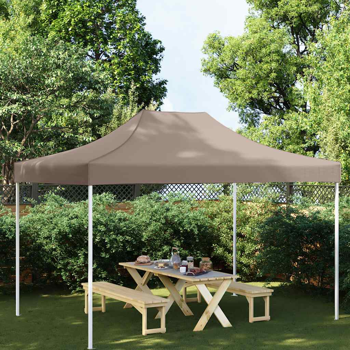 Una tenda marrone con tavolo da picnic e panche in un giardino.