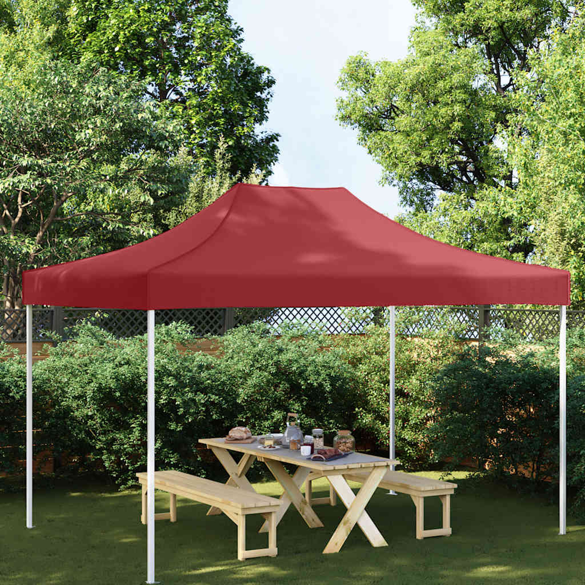 Una tenda rossa ripara un tavolo da picnic in legno con panche e cibo in giardino.