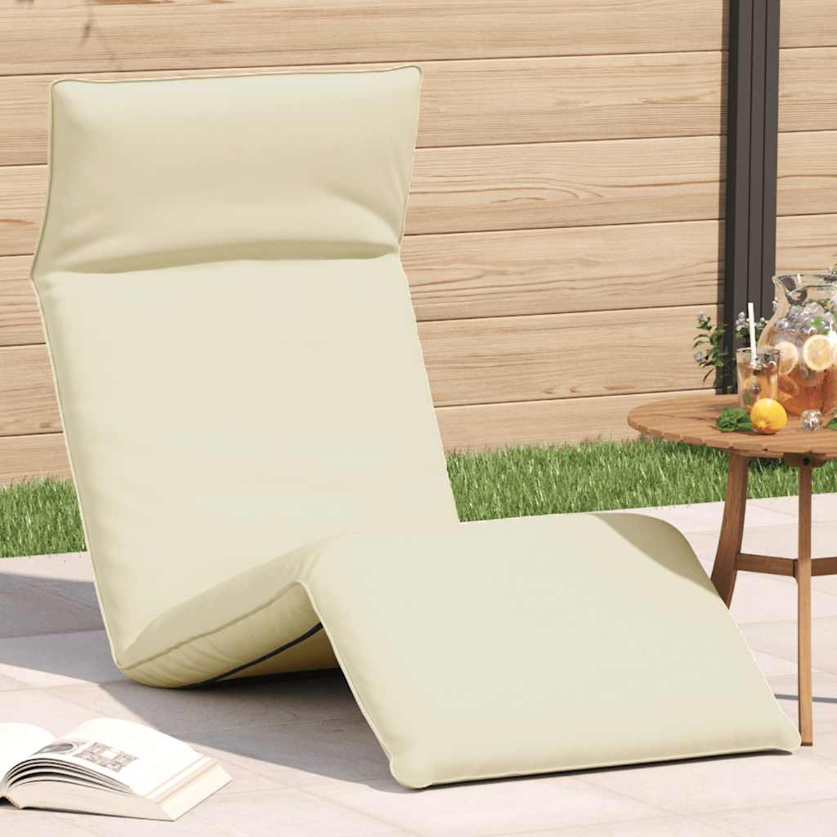 Una poltrona reclinabile beige con cuscini si trova su un patio accanto a una recinzione di legno e un tavolo con bevande.