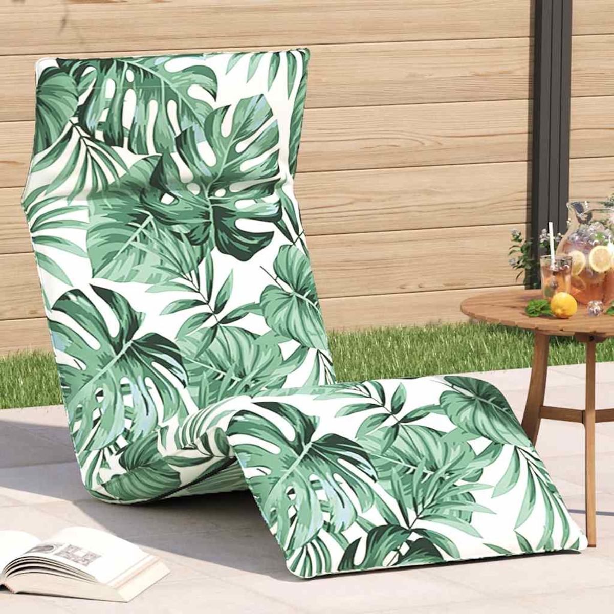 Ein Liegestuhl mit Blattmuster steht auf einer Terrasse neben einem Tisch mit Getränken.