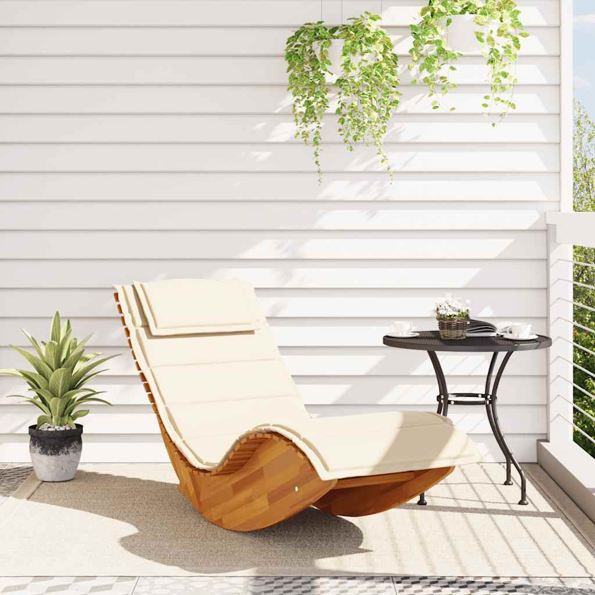 Ein heller Liegestuhl steht auf einem Balkon neben einem kleinen Tisch mit Buch und Tassen.