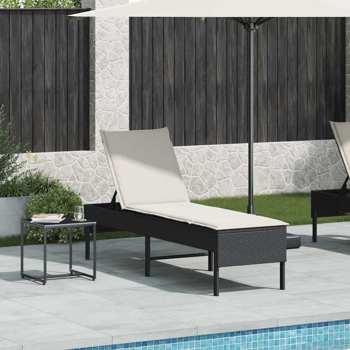 Ein schwarzer Rattan-Liegestuhl mit beiger Polsterung steht auf einer gefliesten Terrasse neben einem kleinen Tisch.