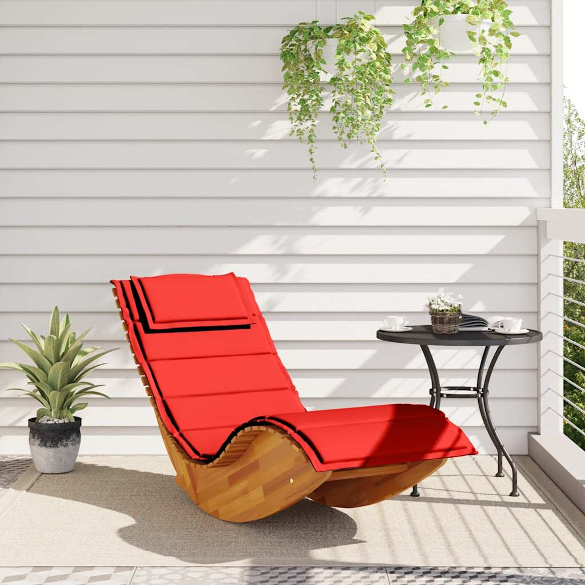 Ein roter Schaukelsessel mit Holzgestell steht auf einer Terrasse neben einem kleinen Tisch.
