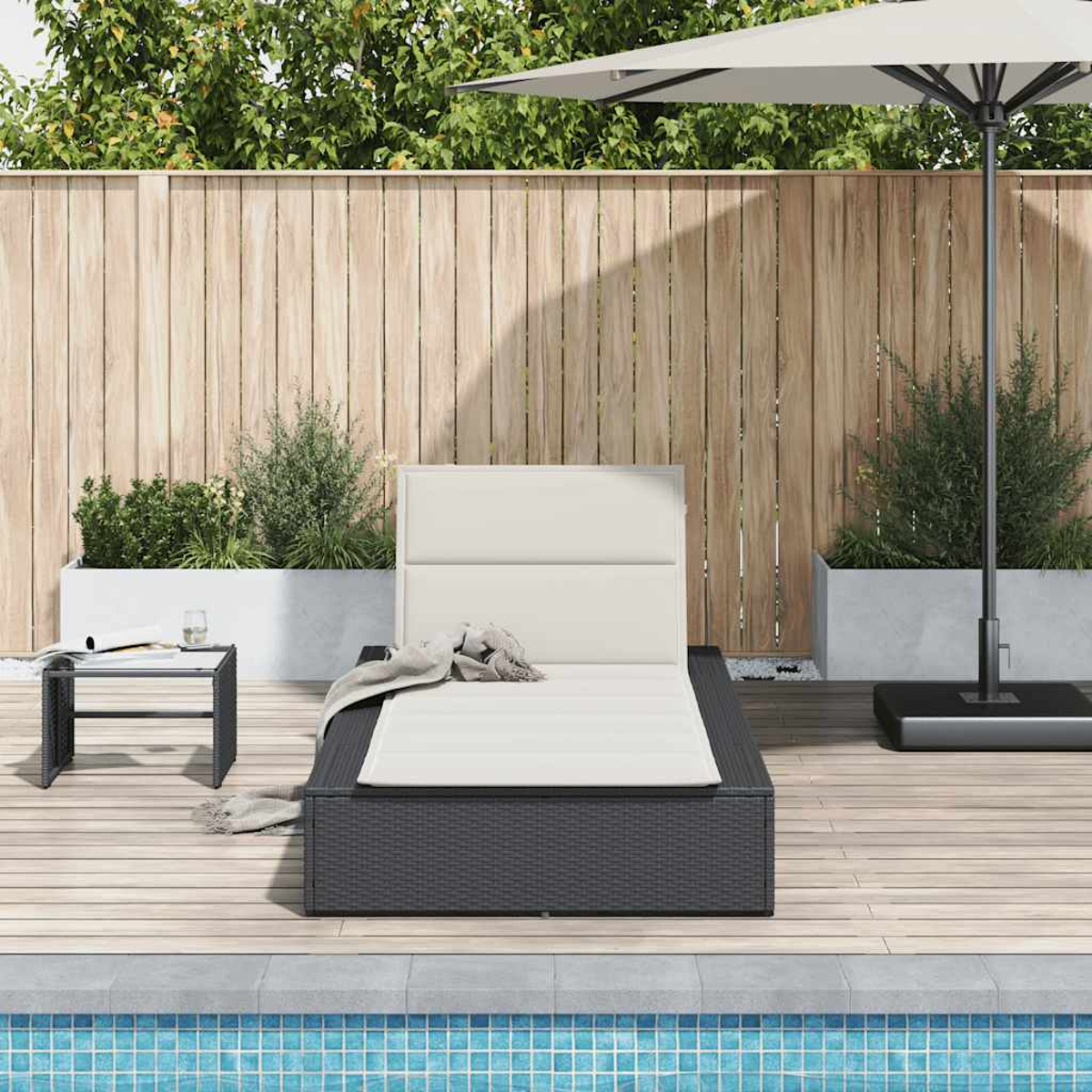 Una chaise longue in vimini scuro con cuscino bianco è vicino alla piscina.