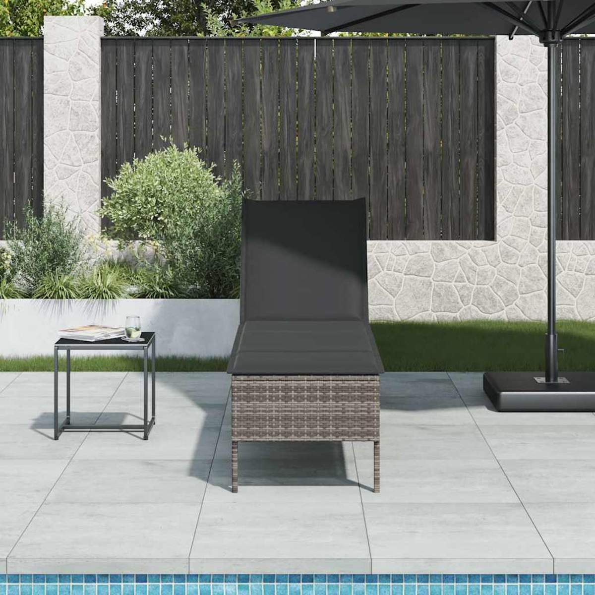 Una chaise longue scura su un patio pavimentato, accanto a un tavolino e un ombrellone.
