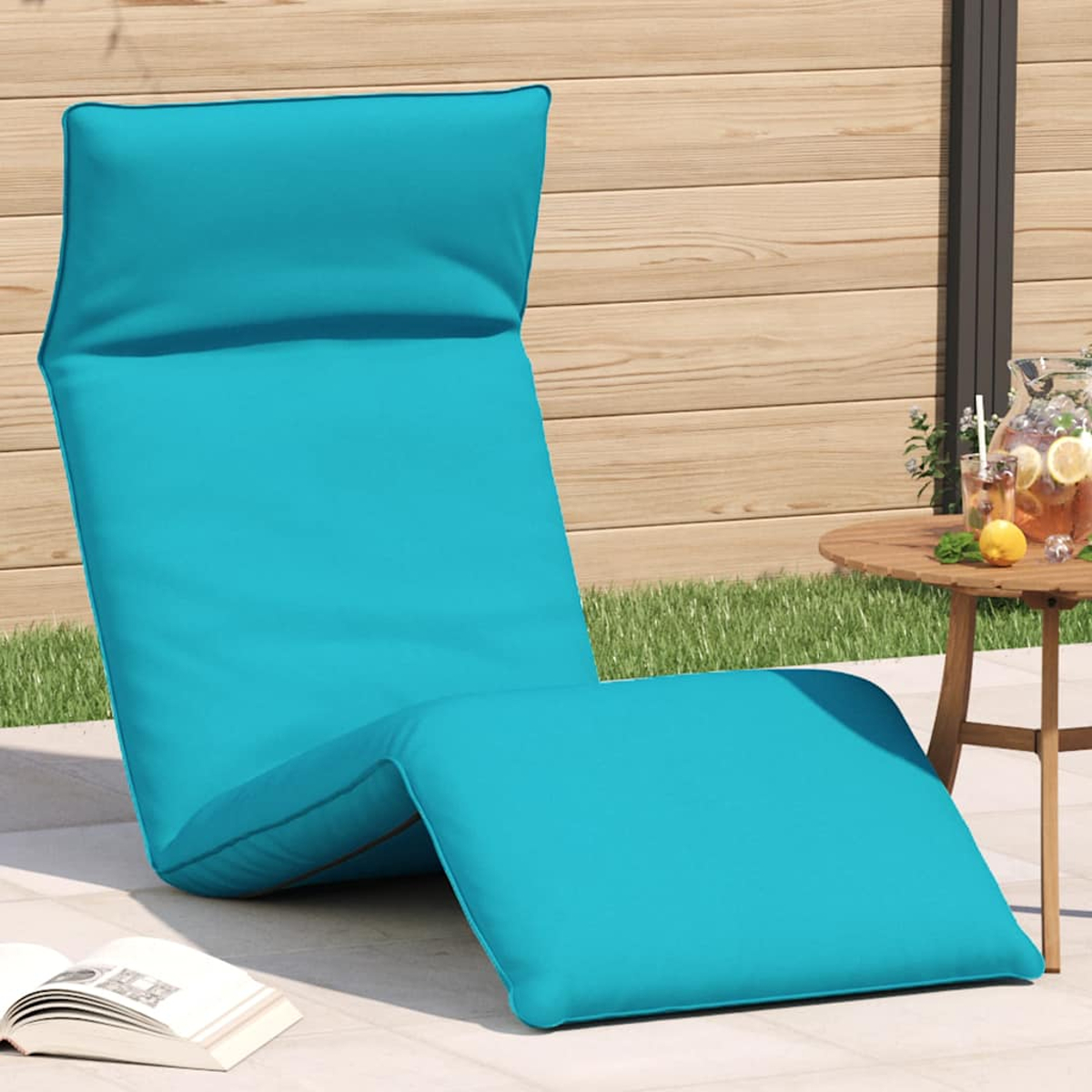 Ein türkisfarbener Liegestuhl steht auf einer Terrasse neben einem Holztisch mit Getränken.