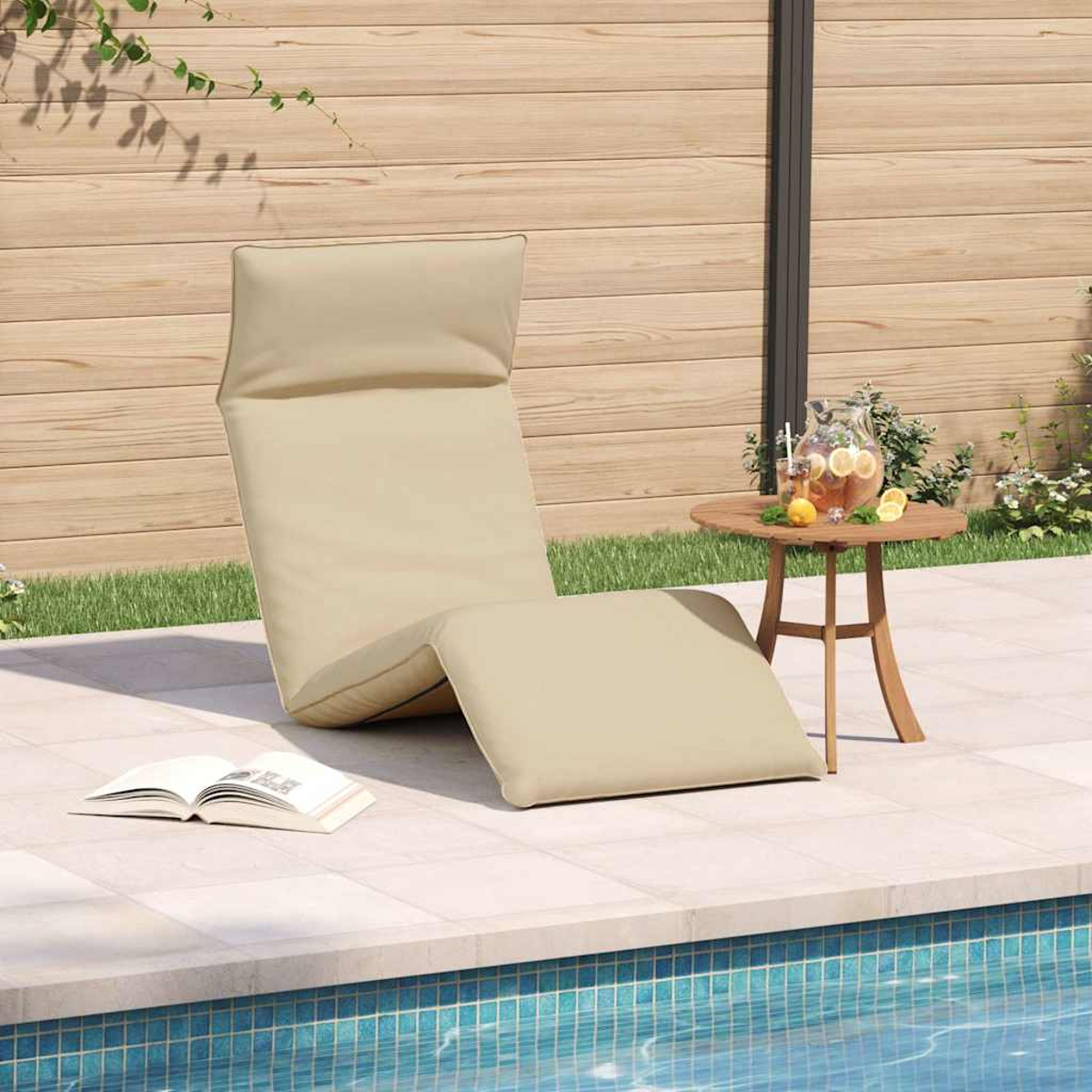 Una chaise longue beige vicino a una piscina, con un tavolino di legno che tiene una brocca di limonata.