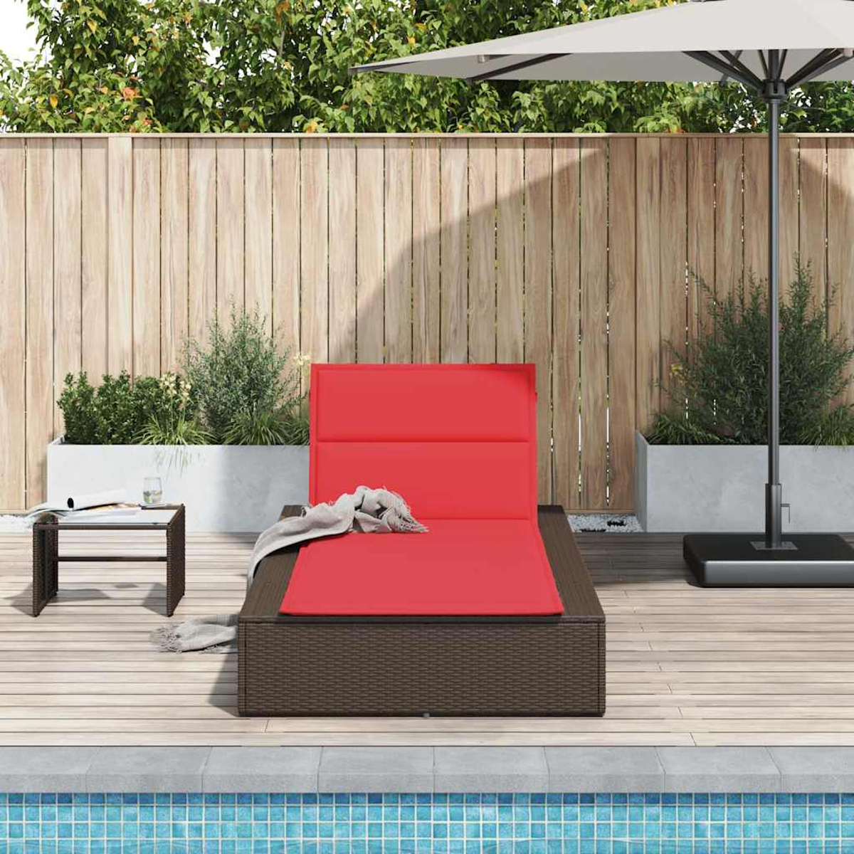 Lettino rosso con coperta grigia su ponte di legno vicino alla piscina, con piante e ombrellone.